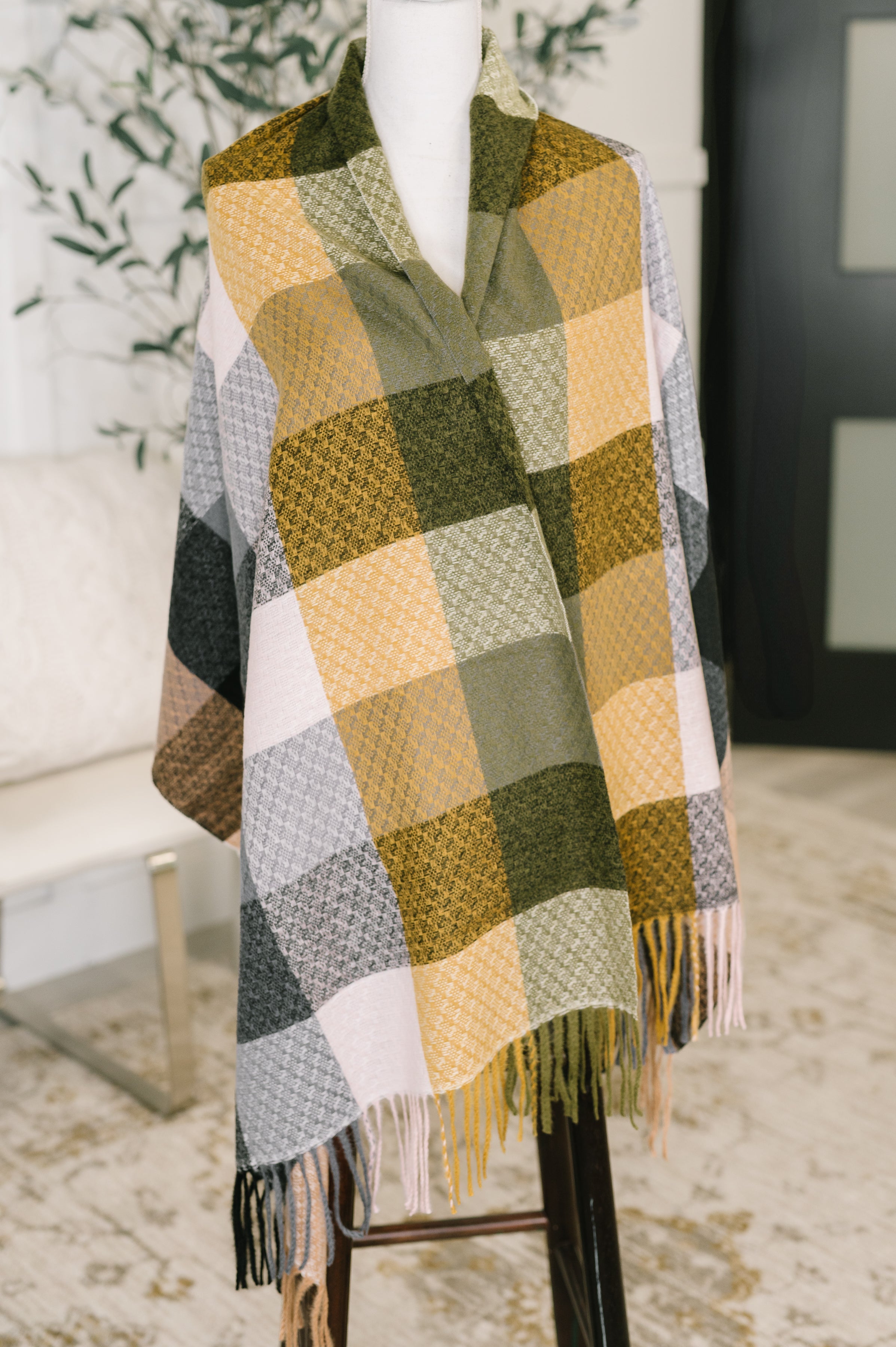 Colorful checkered scarf with fringe draped over a dress form in an indoor setting.