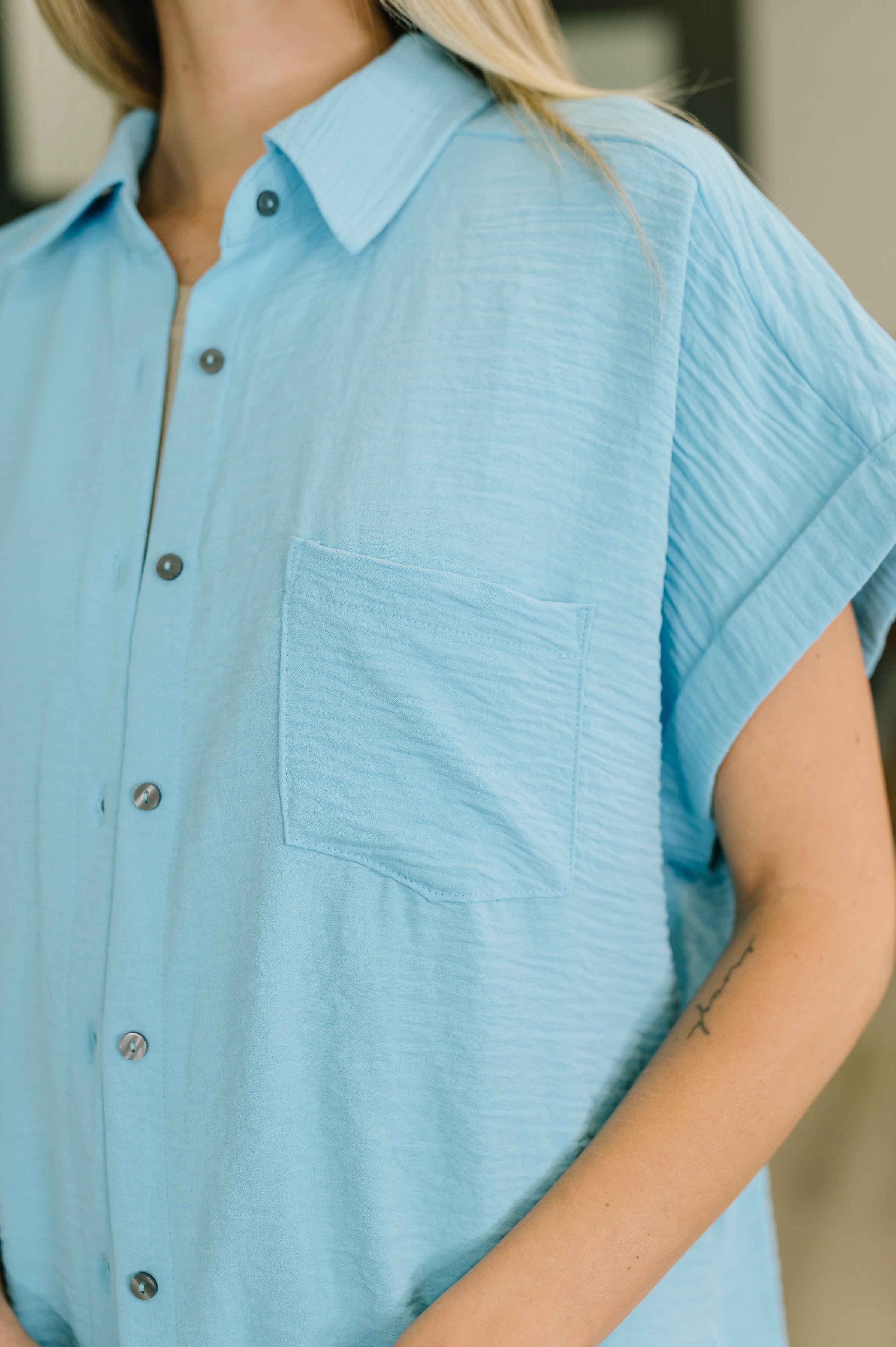 Close-up of woman wearing textured sky blue short sleeve button-down shirt with chest pocket and rolled cuffs indoors