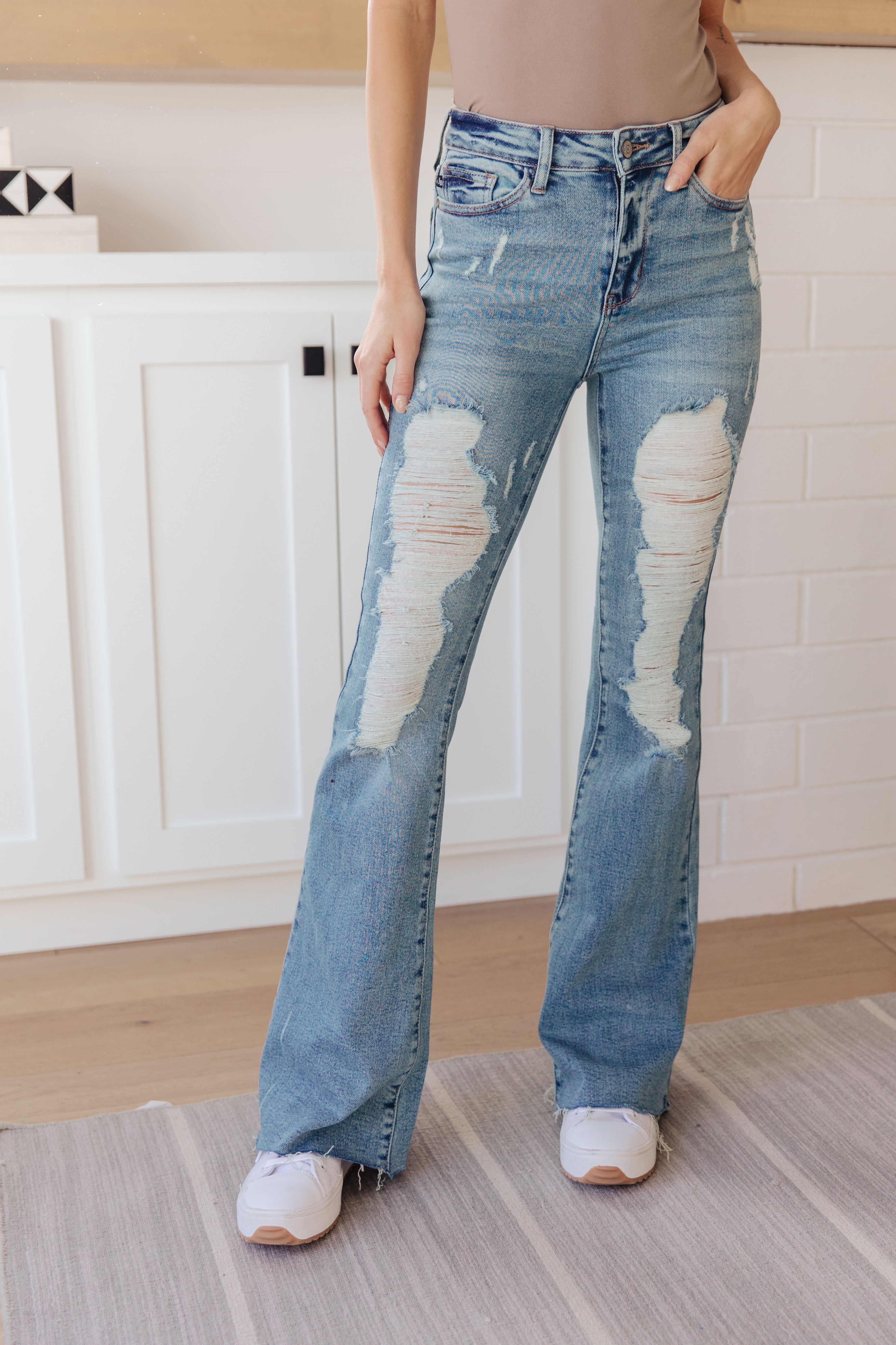 Person wearing blue high-rise distressed flare jeans paired with white sneakers indoors standing on a rug