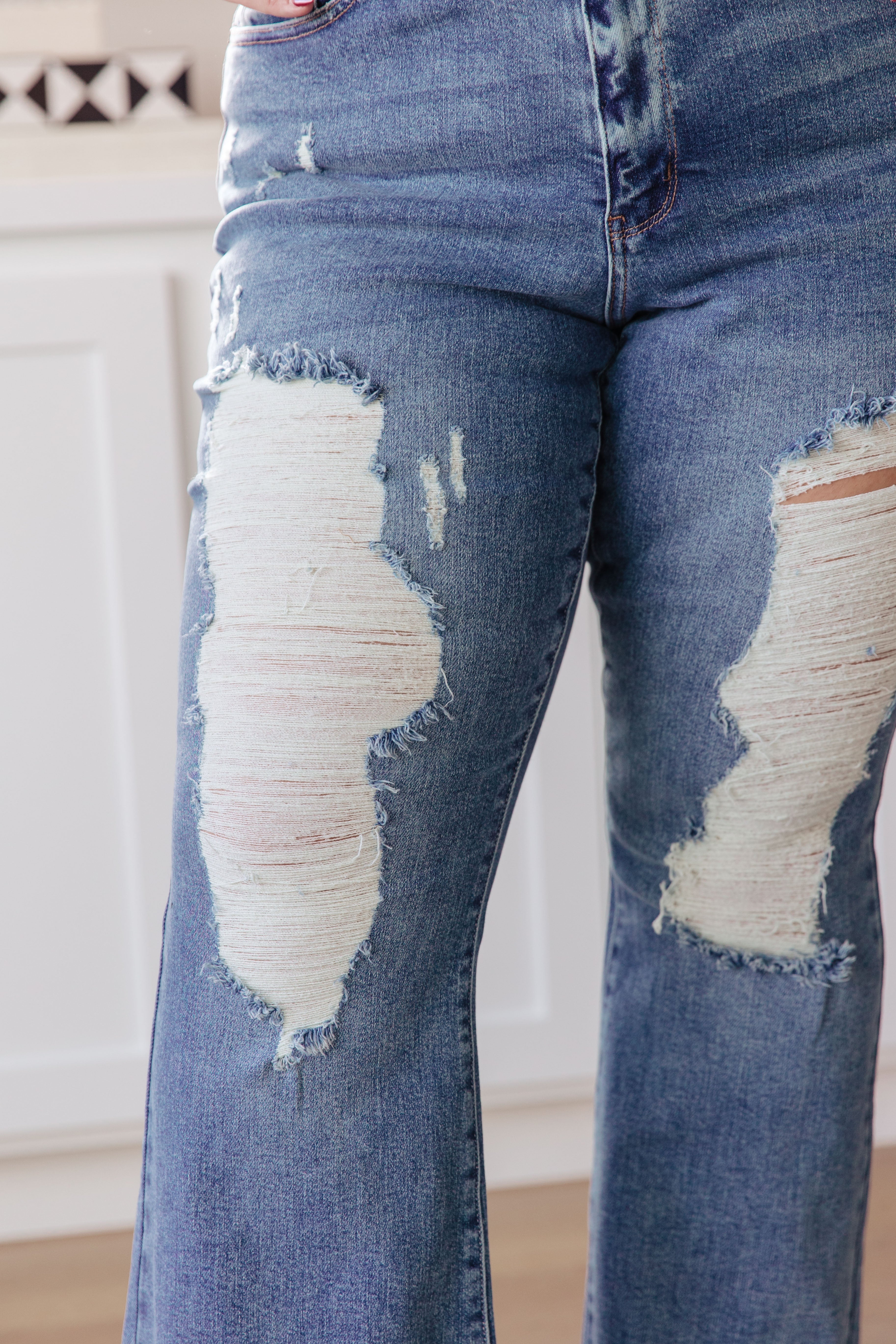 Close-up of blue high-rise jeans with heavy distressing and frayed patches on thighs and flare legs indoors