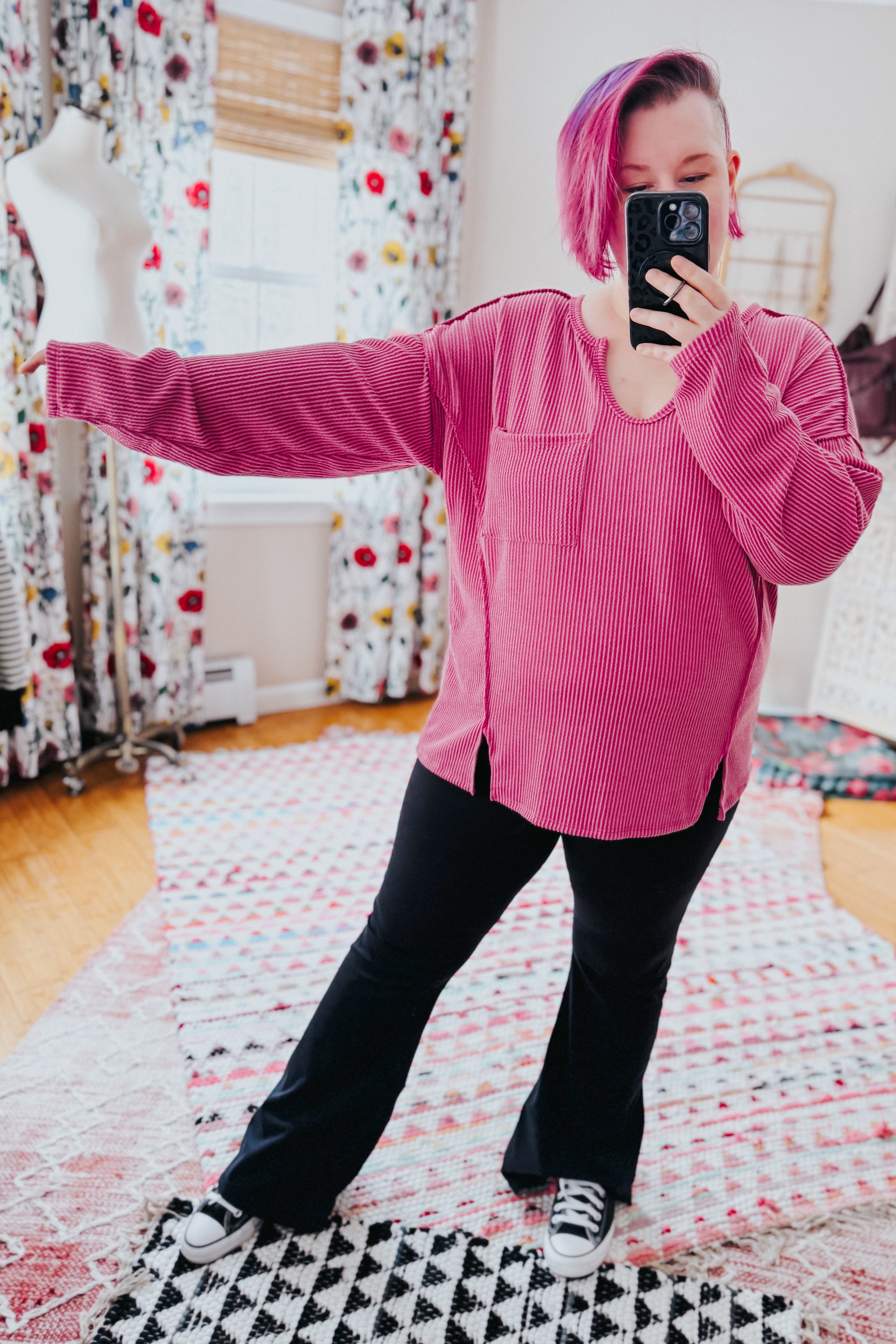 Woman with short pink hair wearing a loose magenta ribbed top with front pocket and side slits taking a selfie indoors