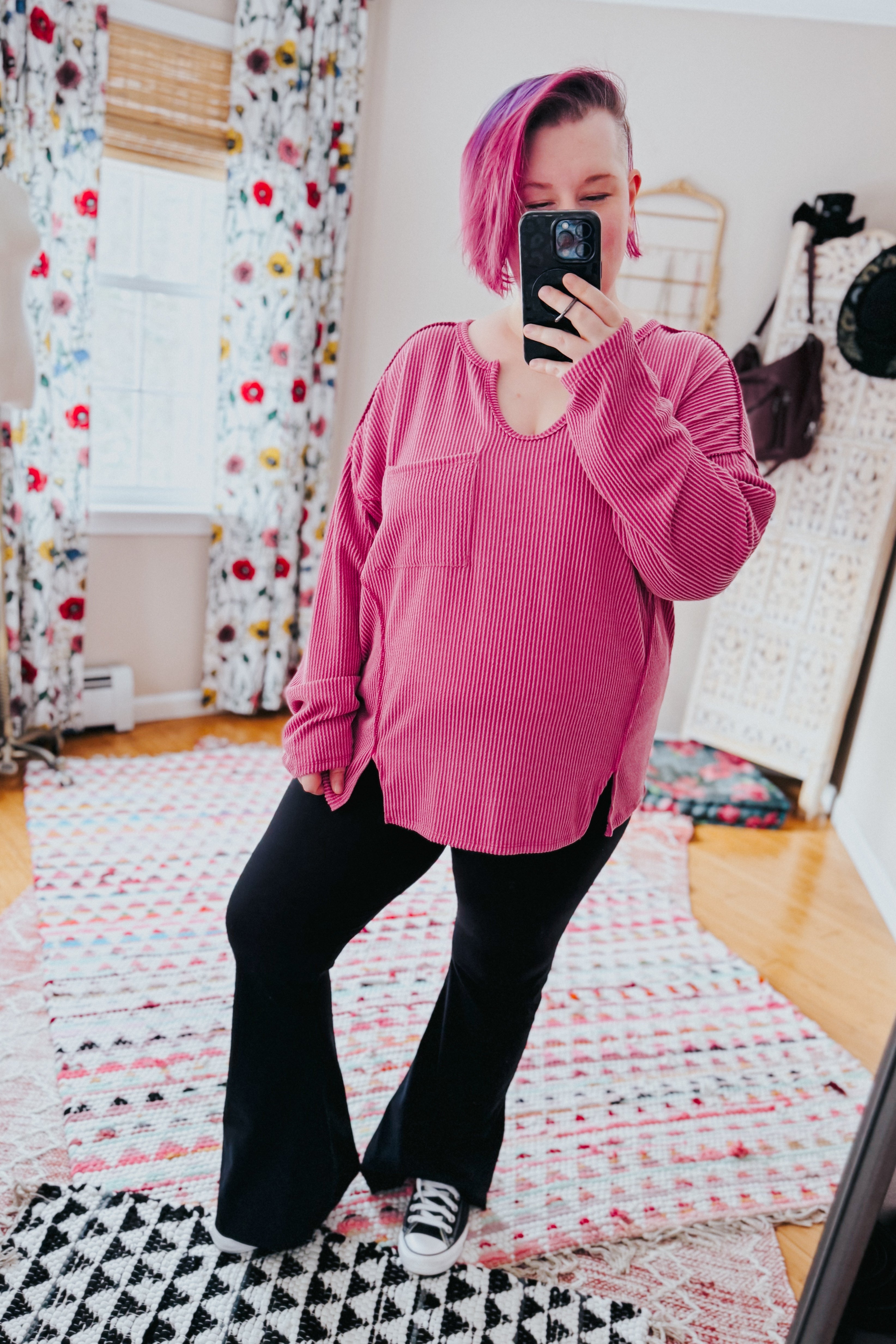 Woman with short purple hair wearing loose magenta ribbed top with front pocket and side slits taking a mirror selfie indoors