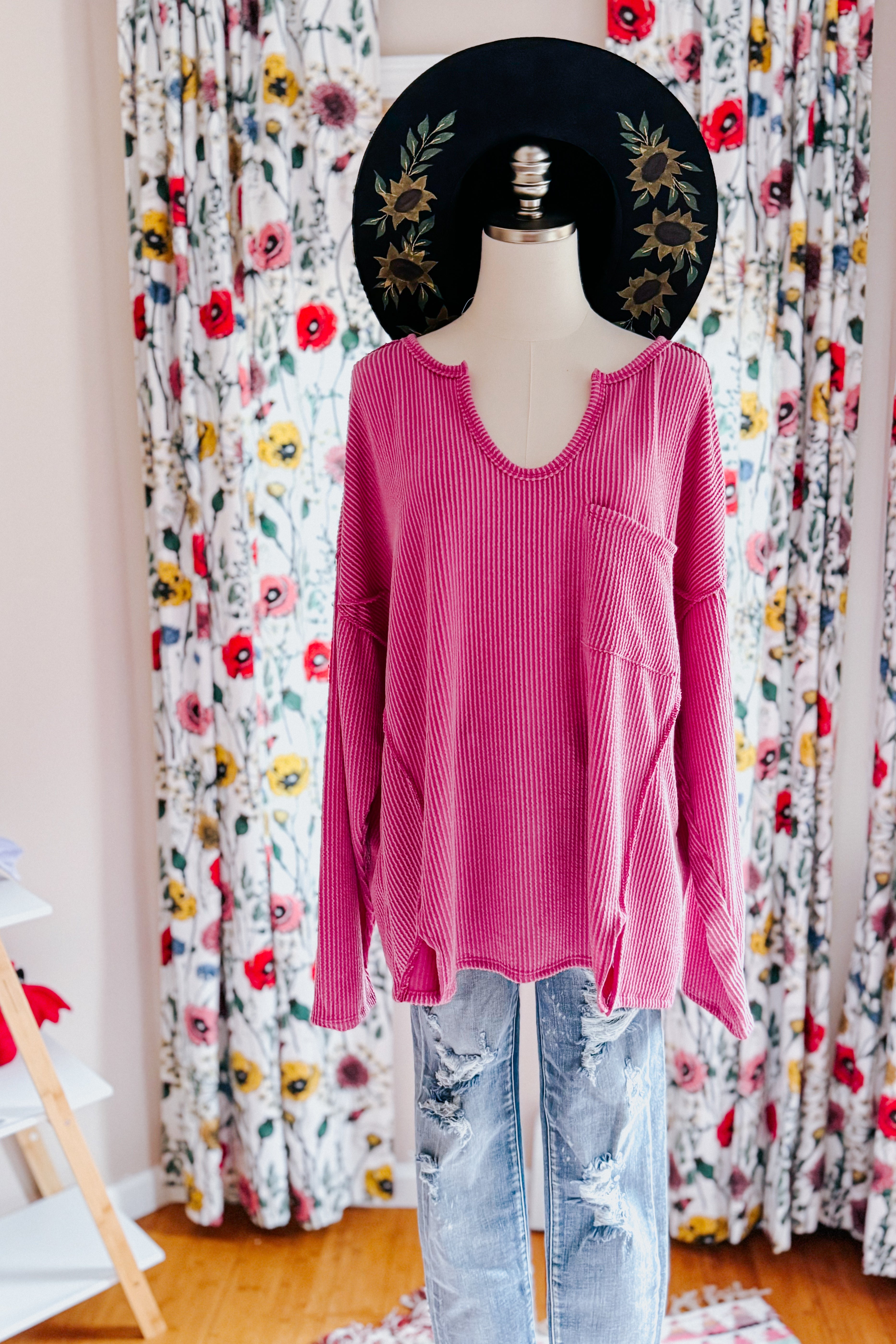 Magenta ribbed long sleeve top with front pocket and distressed light wash jeans displayed on mannequin with floral curtains background