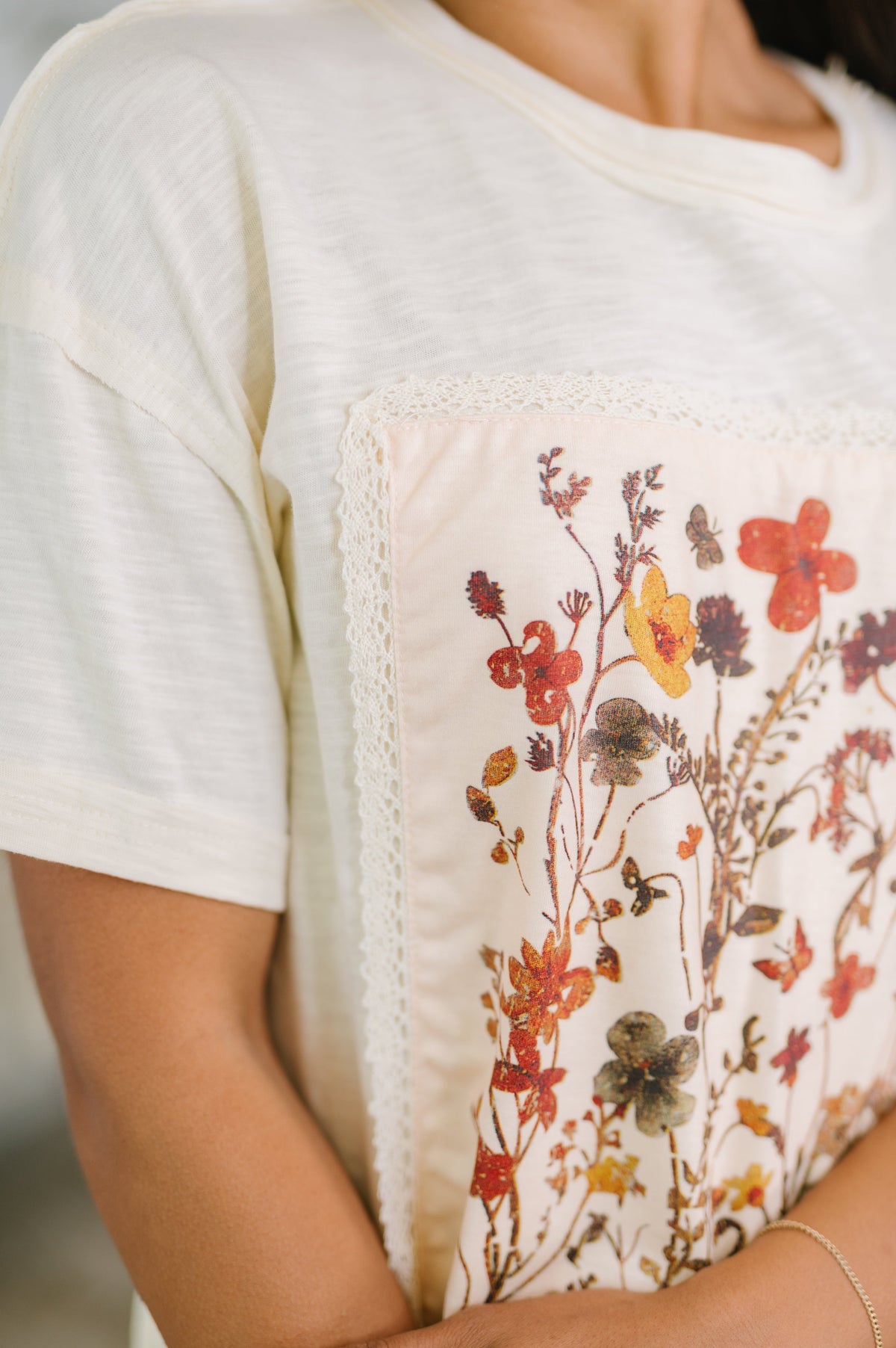 Woman wearing an ivory knit top with a lace trimmed floral applique panel and short sleeves close up