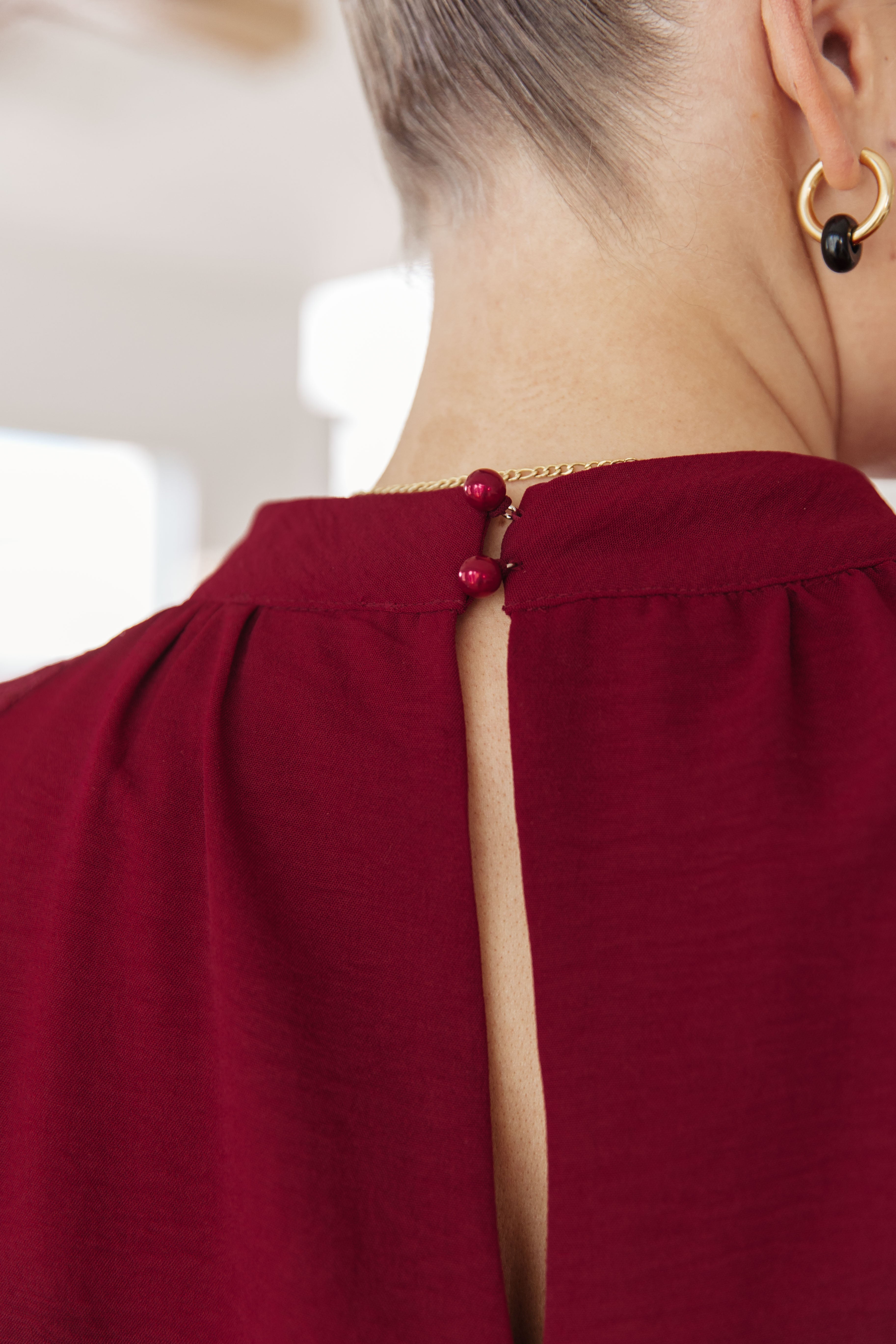 Close-up of the back neckline on a wine-colored blouse with fabric-covered button closures and subtle gathering detail