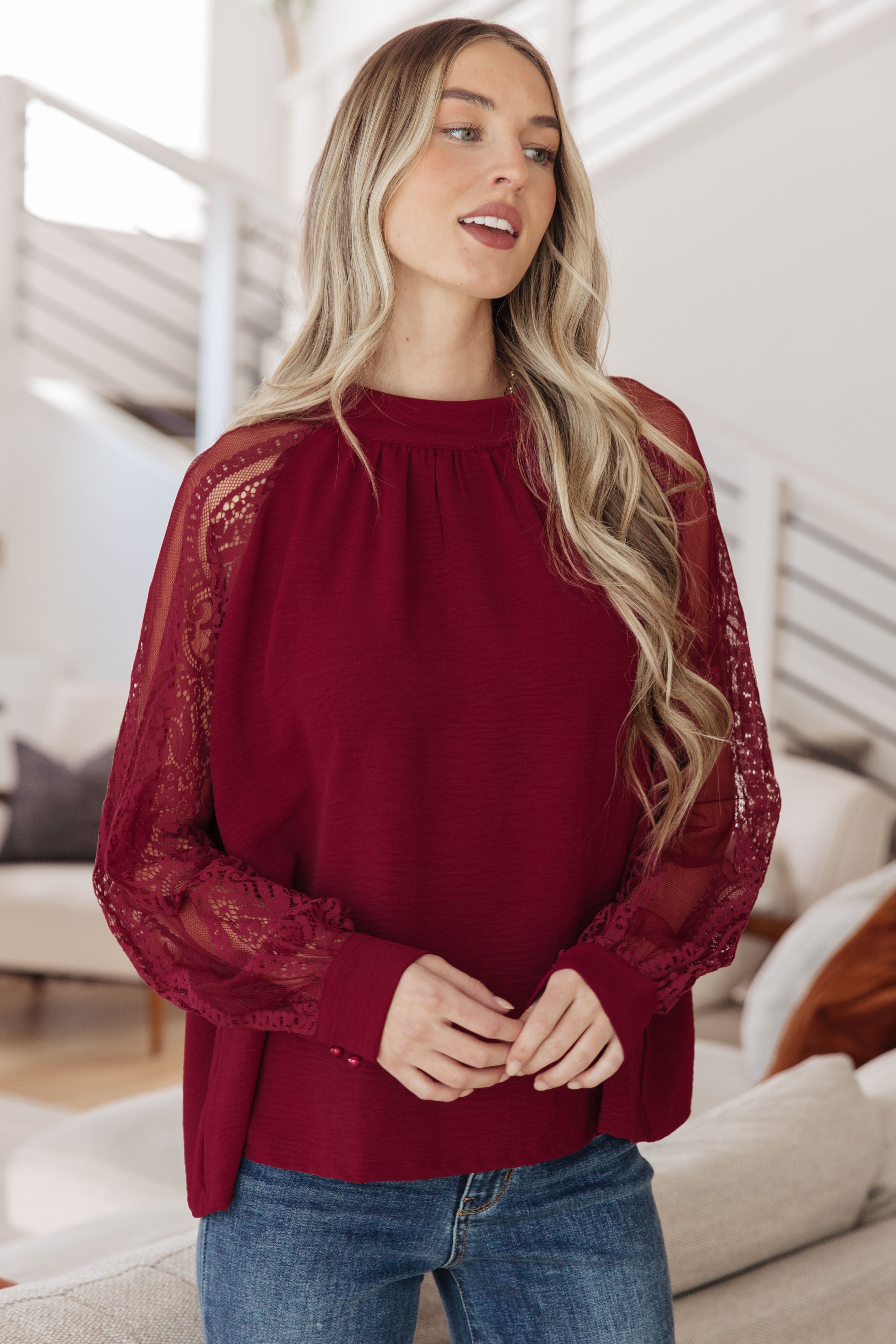 Woman in wine-colored blouse with sheer lace sleeves and gathered neckline indoors with light modern decor