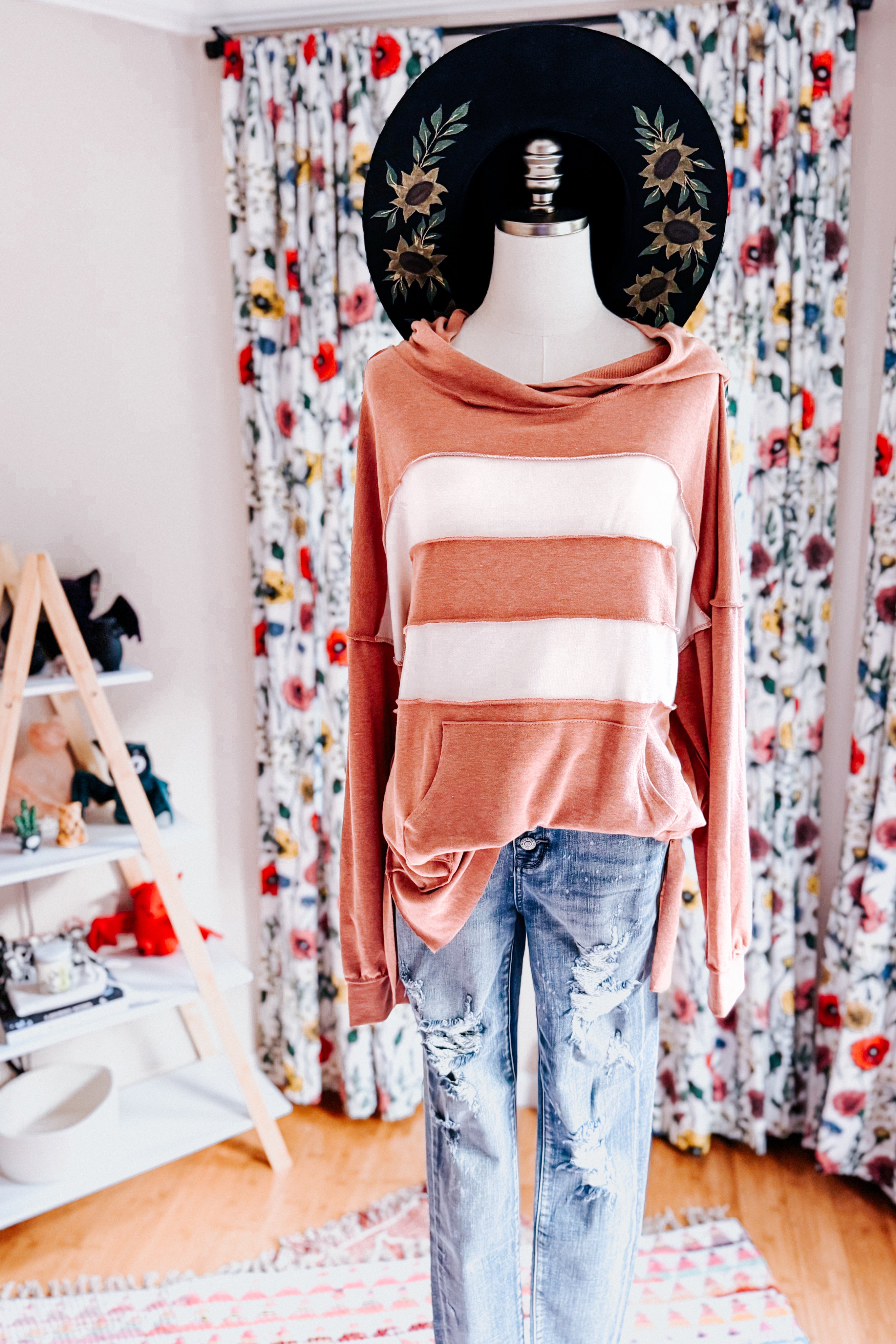 Mannequin wearing a rust-colored hoodie with broad cream stripes and distressed blue jeans indoors