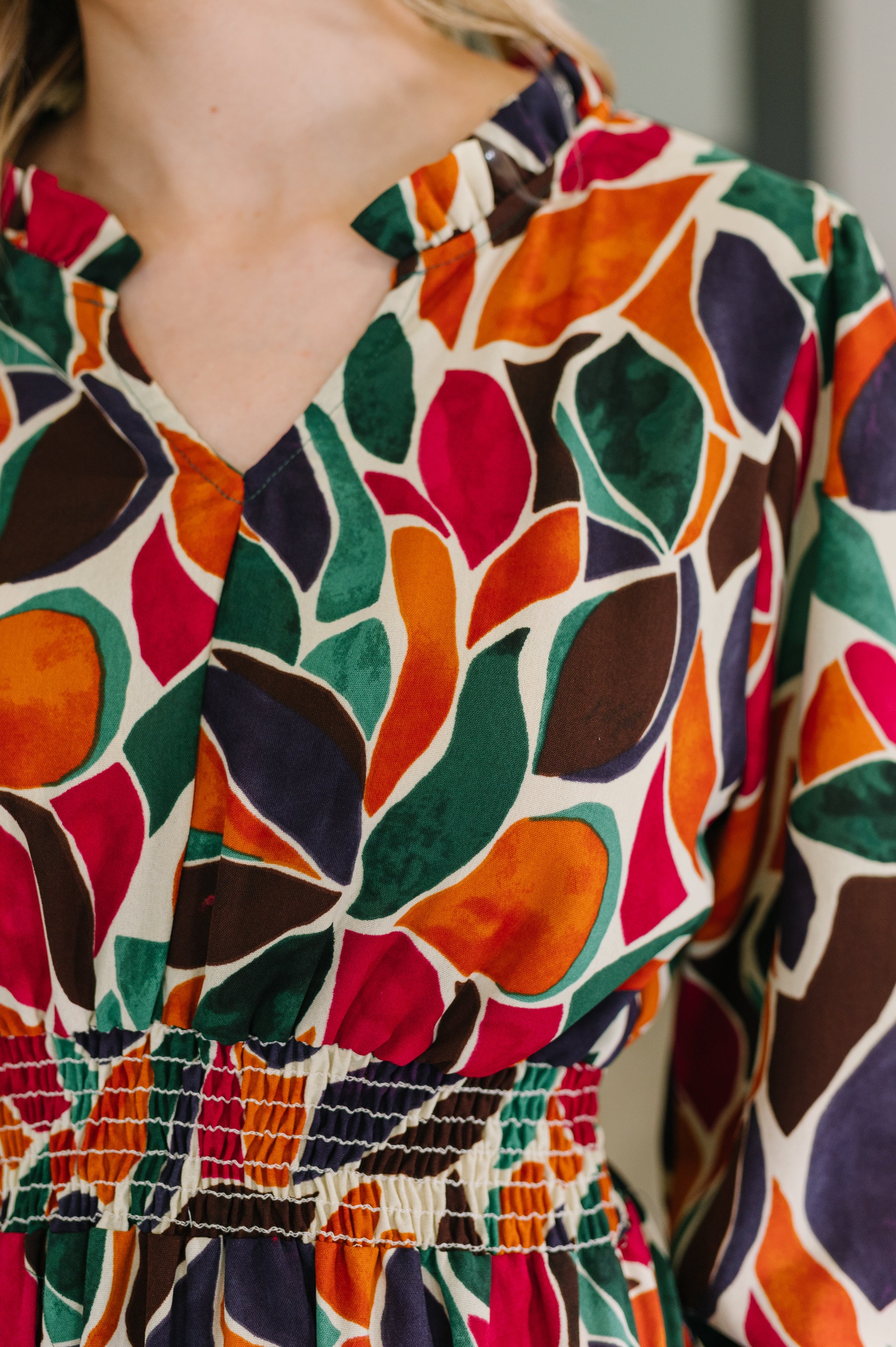 Close-up of long sleeve dress with vibrant red, green, orange, and purple leaf-like abstract pattern and gathered waist detail