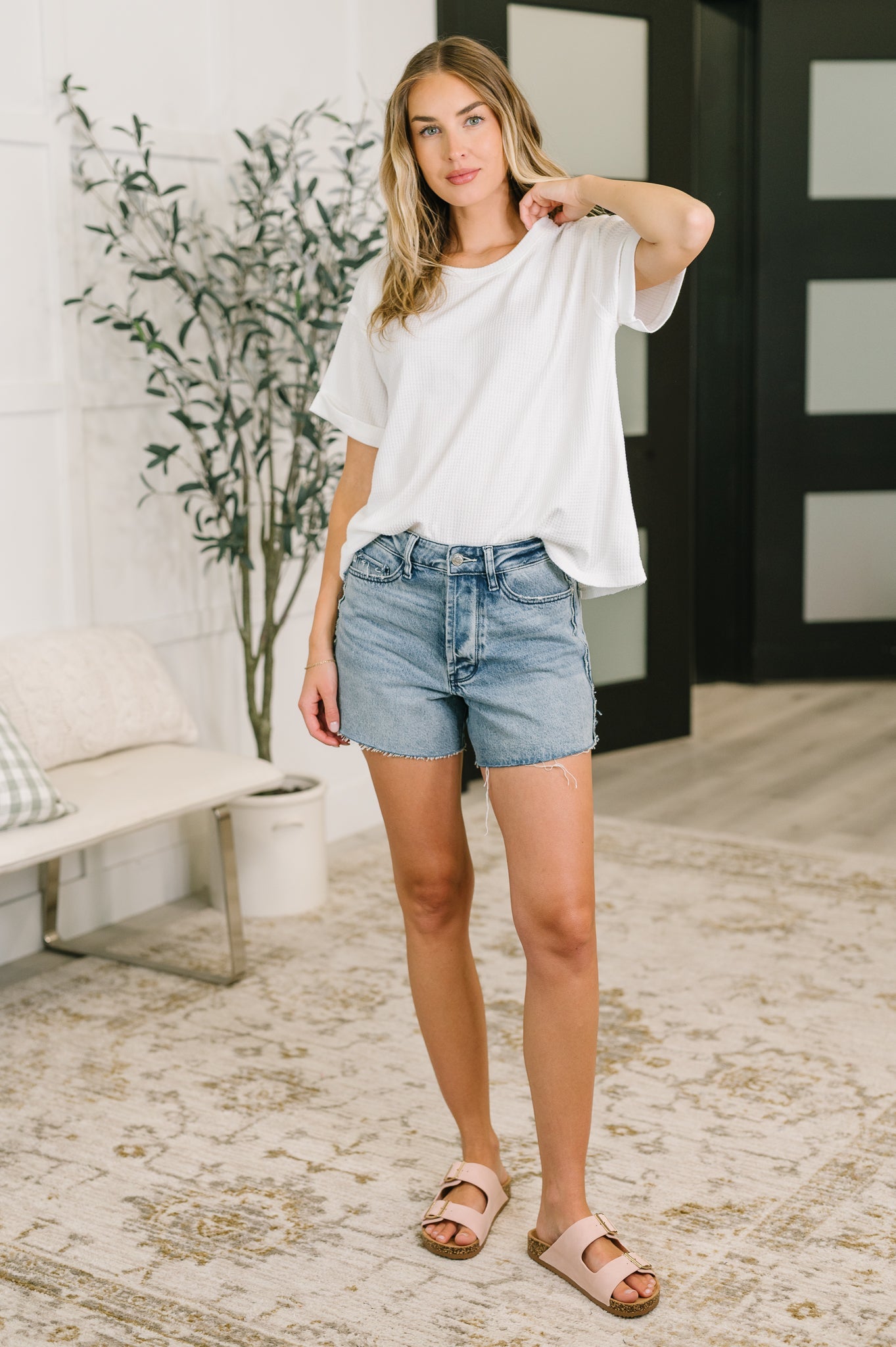 Woman wearing relaxed ivory waffle knit tee with light denim shorts and sandals in a cozy eclectic room