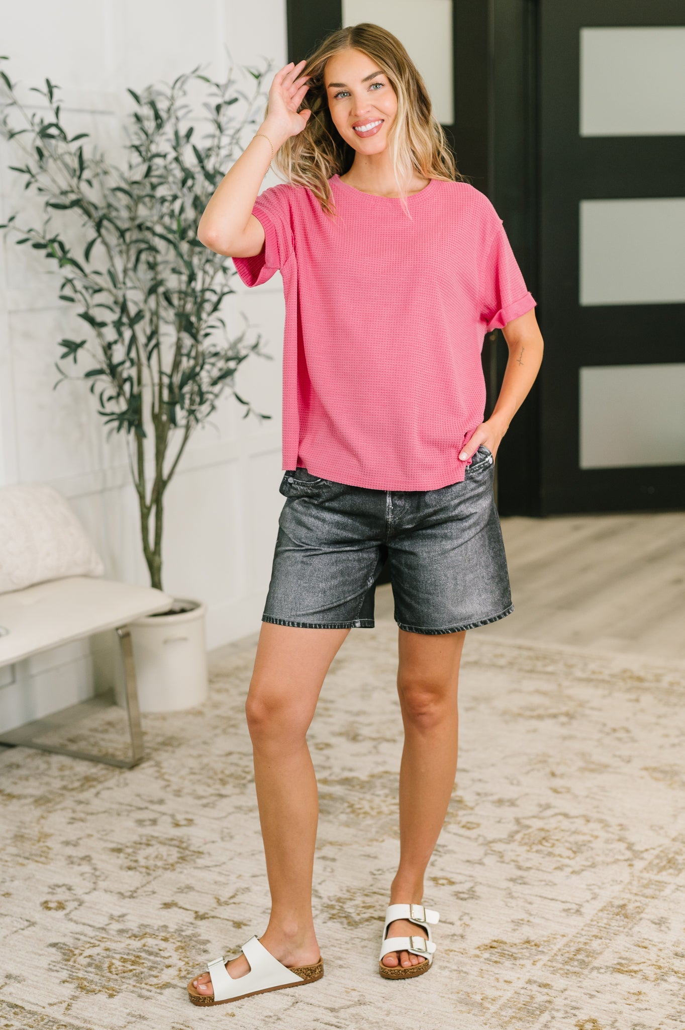 Woman wearing relaxed pink waffle knit tee paired with black casual shorts and white sandals in eclectic room