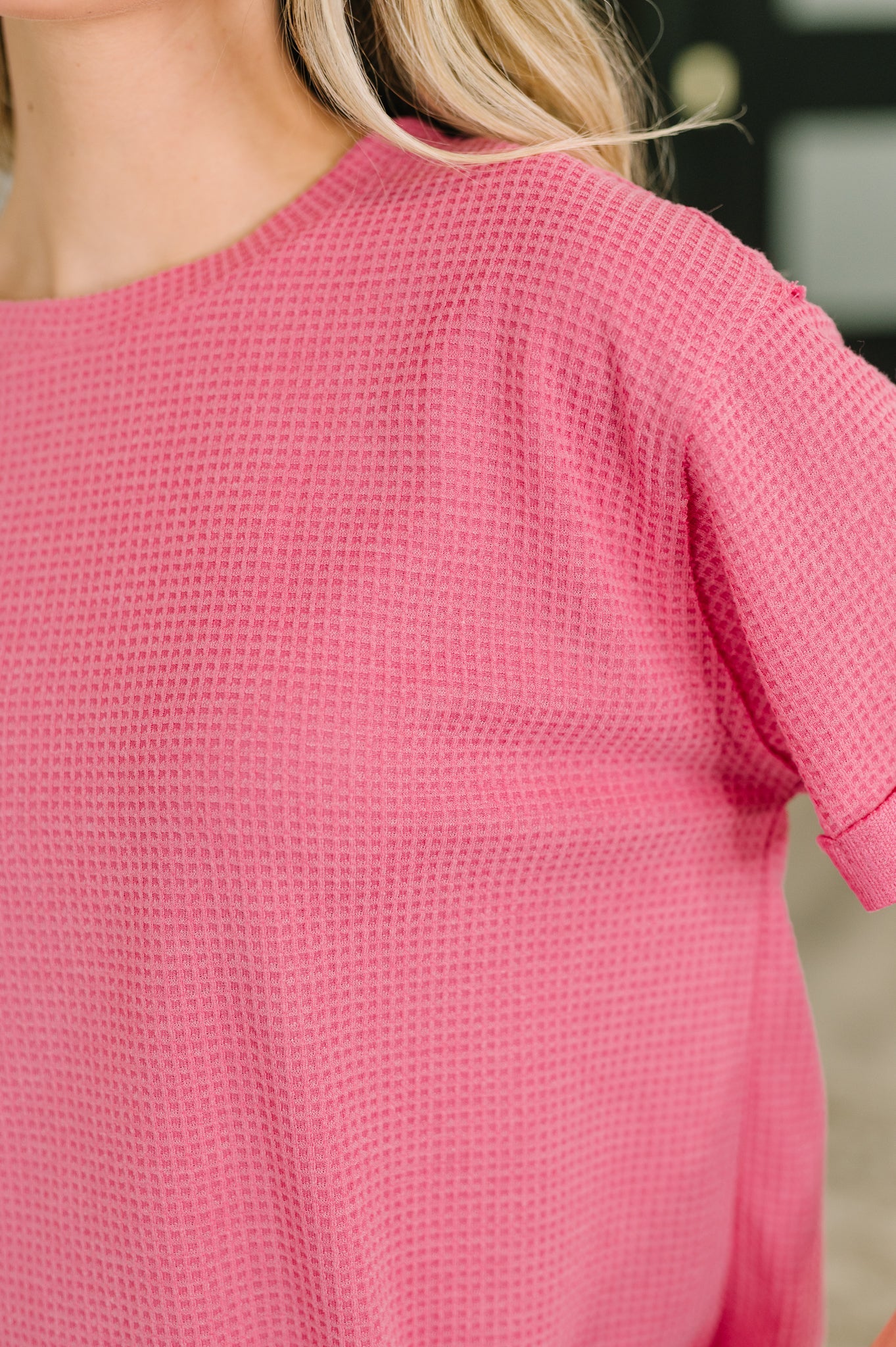 Close-up of soft pink waffle knit fabric with textured pattern and relaxed short sleeve in bright setting