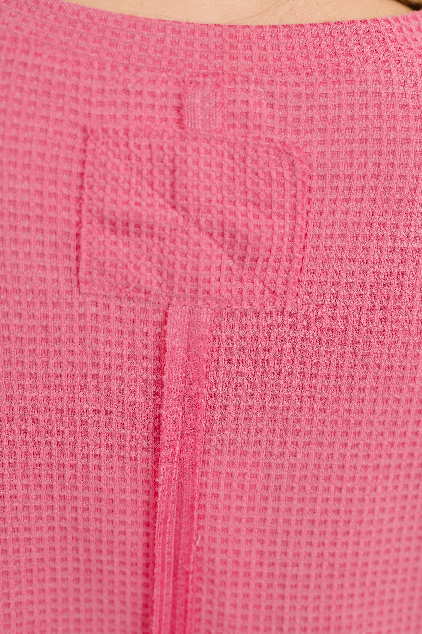 Close-up of textured pink waffle knit fabric with stitched detail, showcasing soft and cozy material quality