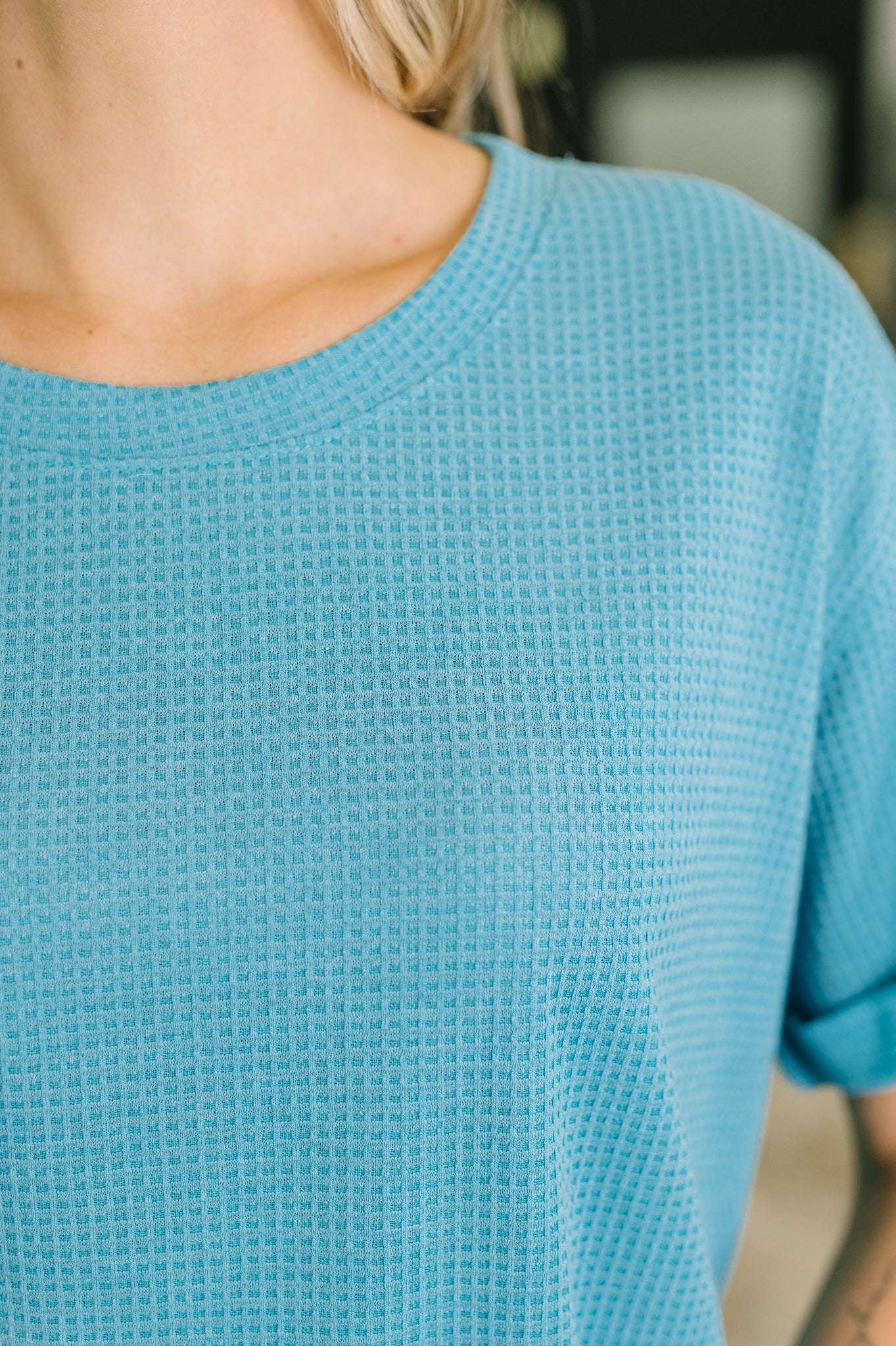 Close-up of teal waffle knit fabric on relaxed tee with soft texture and rolled sleeve in bright setting