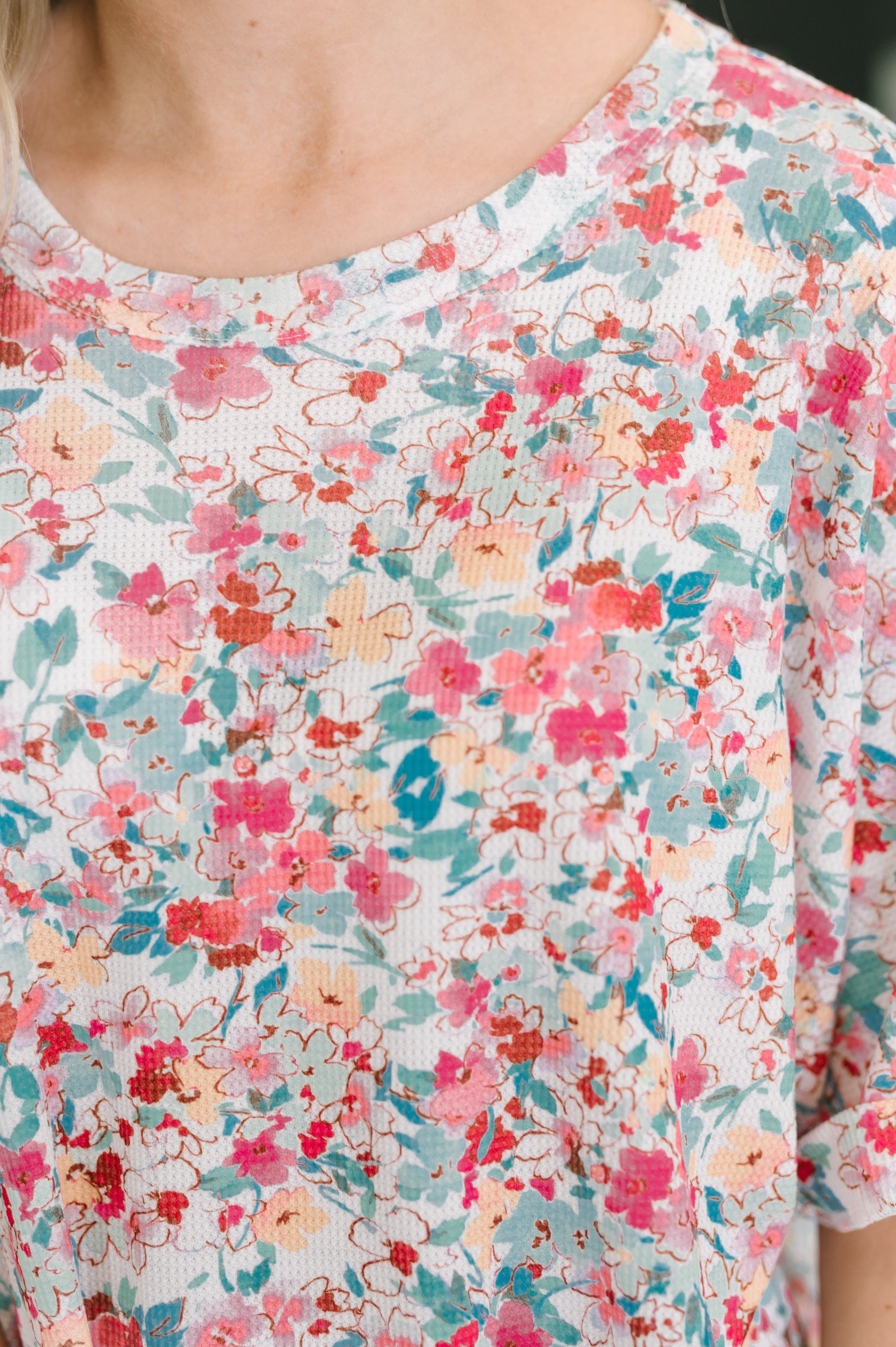 Close-up of pink waffle knit fabric blouse with vibrant floral print and banded round neckline on lightweight material