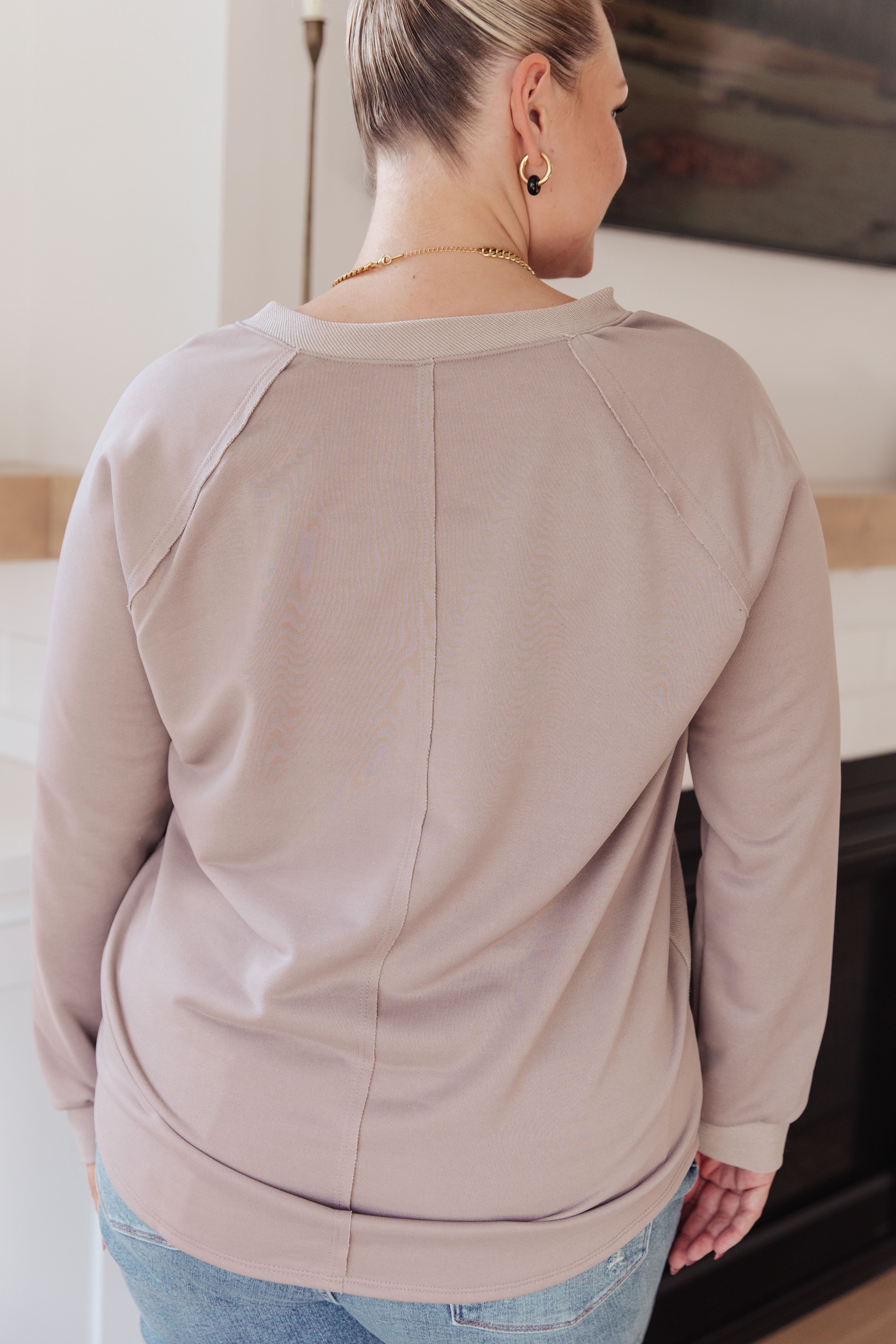 Woman wearing a beige long sleeve top with seam details on the back, paired with light wash jeans, indoors