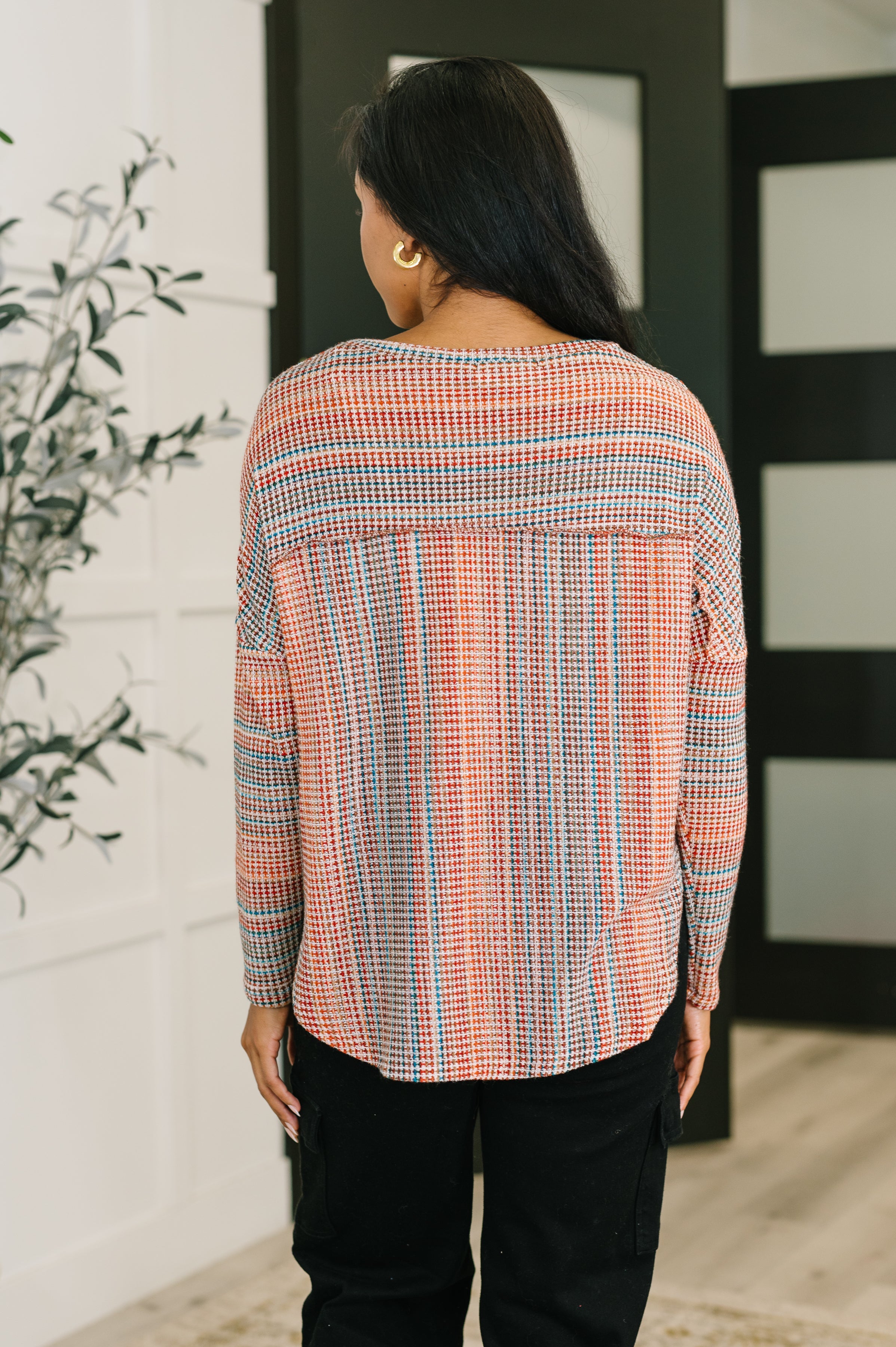 Woman seen from behind wearing a long sleeve orange patterned top with vertical and horizontal stripes indoors