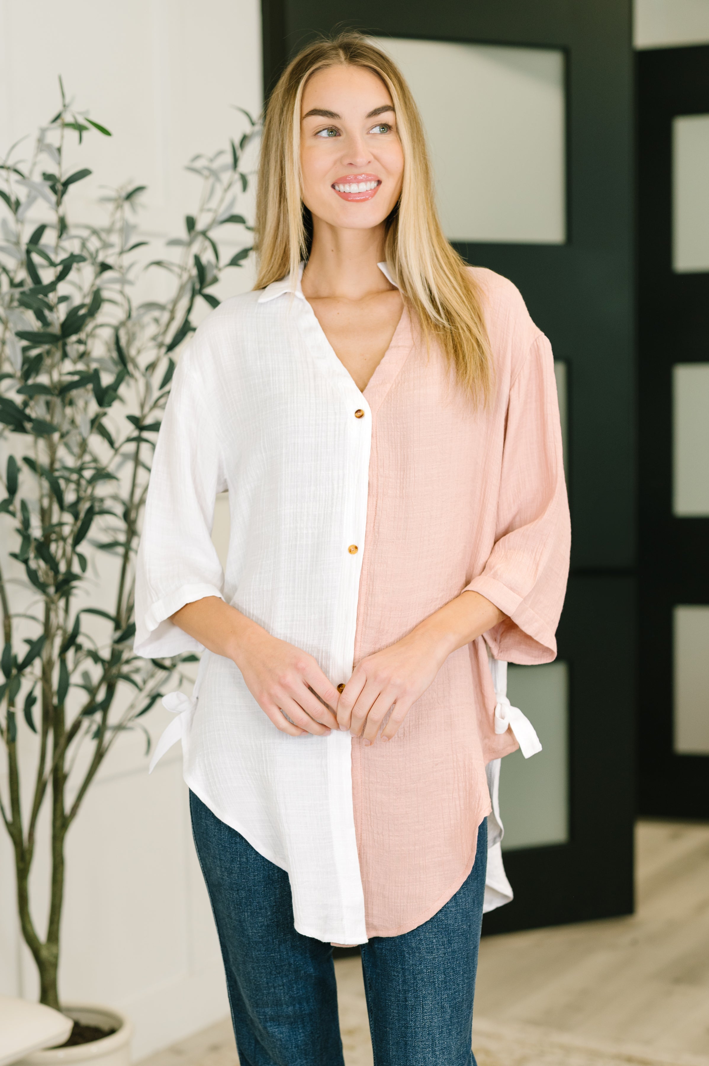 Woman wearing a relaxed dual-tone button-down shirt in white and blush pink with side ties paired with dark jeans indoors