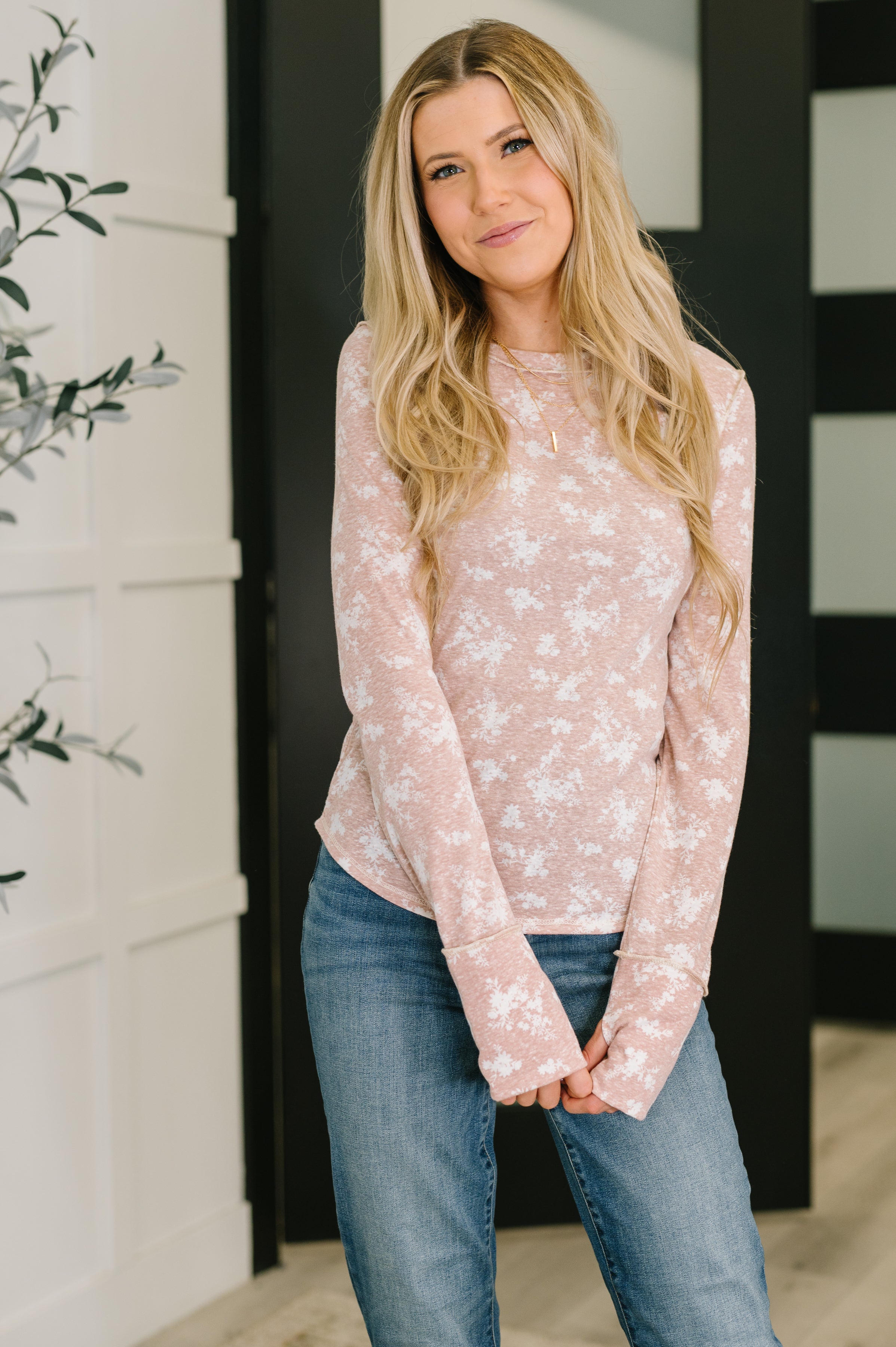 Woman wearing a soft pink floral long-sleeve top paired with blue jeans standing inside a modern room