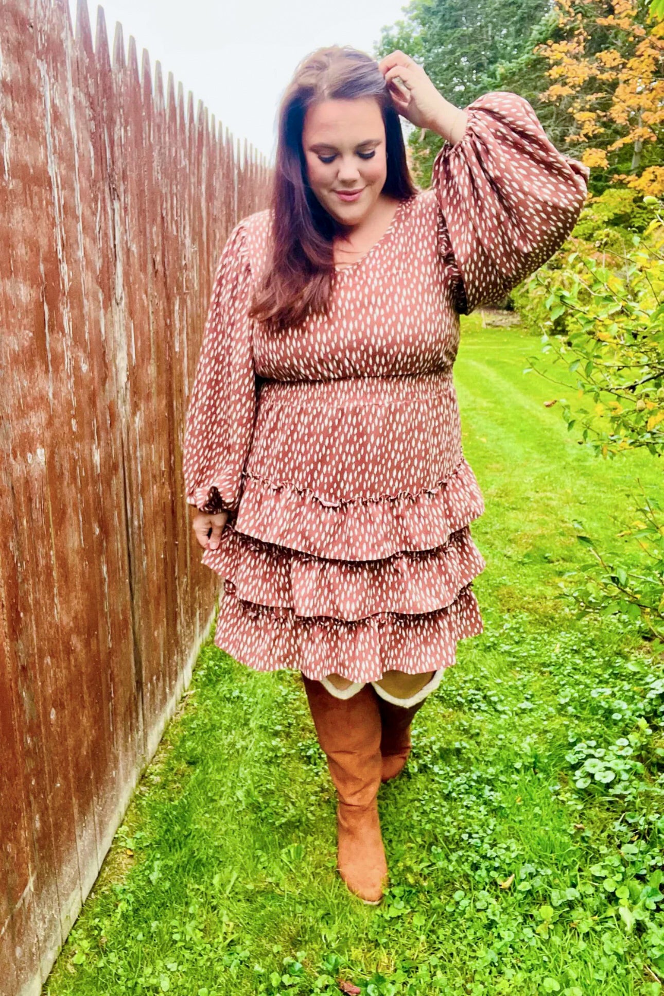 Woman outdoors wearing a terracotta dress with white dash pattern, smocked waist, balloon sleeves, and tiered ruffle skirt with knee-high boots