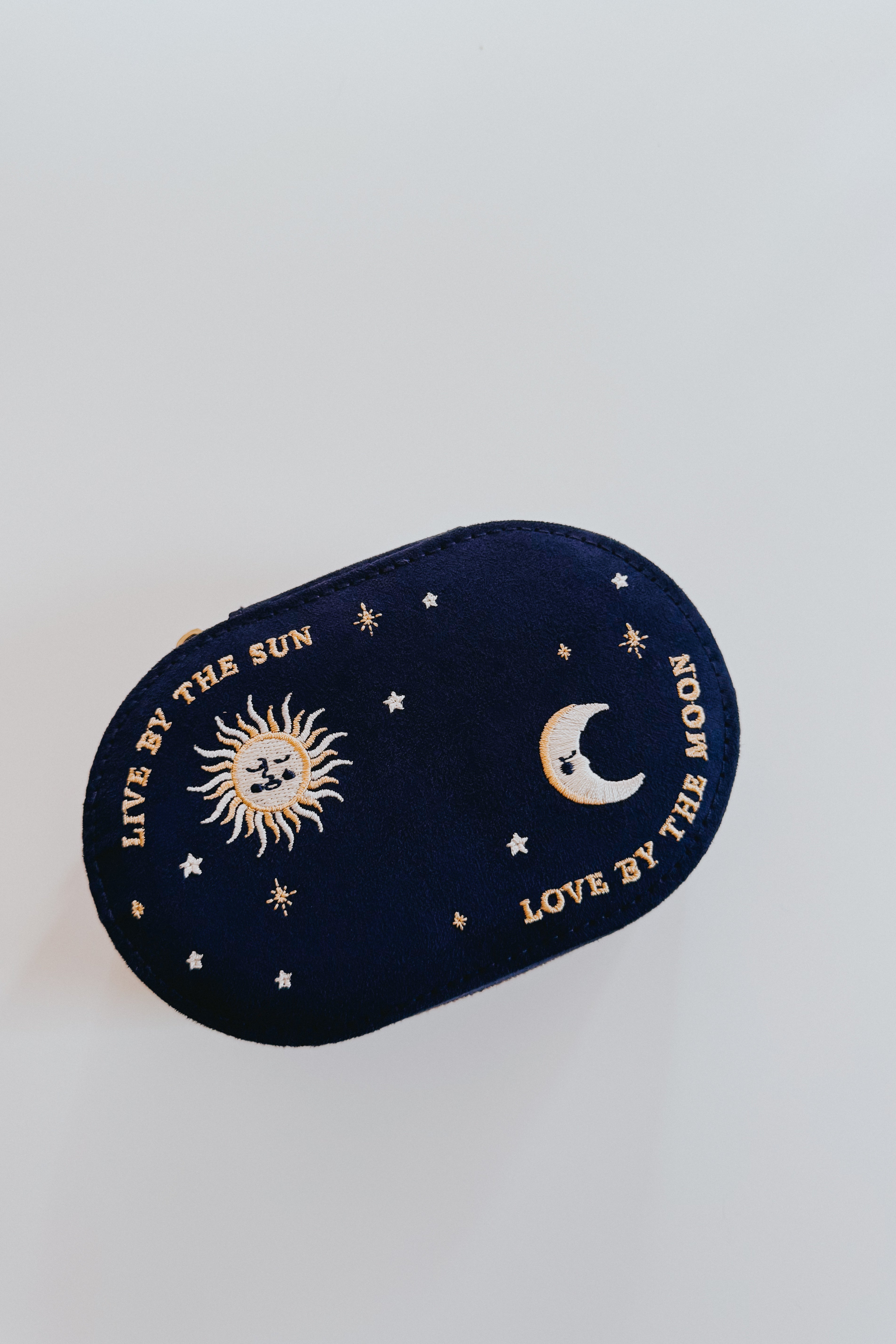 Navy blue oval jewelry box embroidered with a sun, moon, stars, and the phrase live by the sun love by the moon