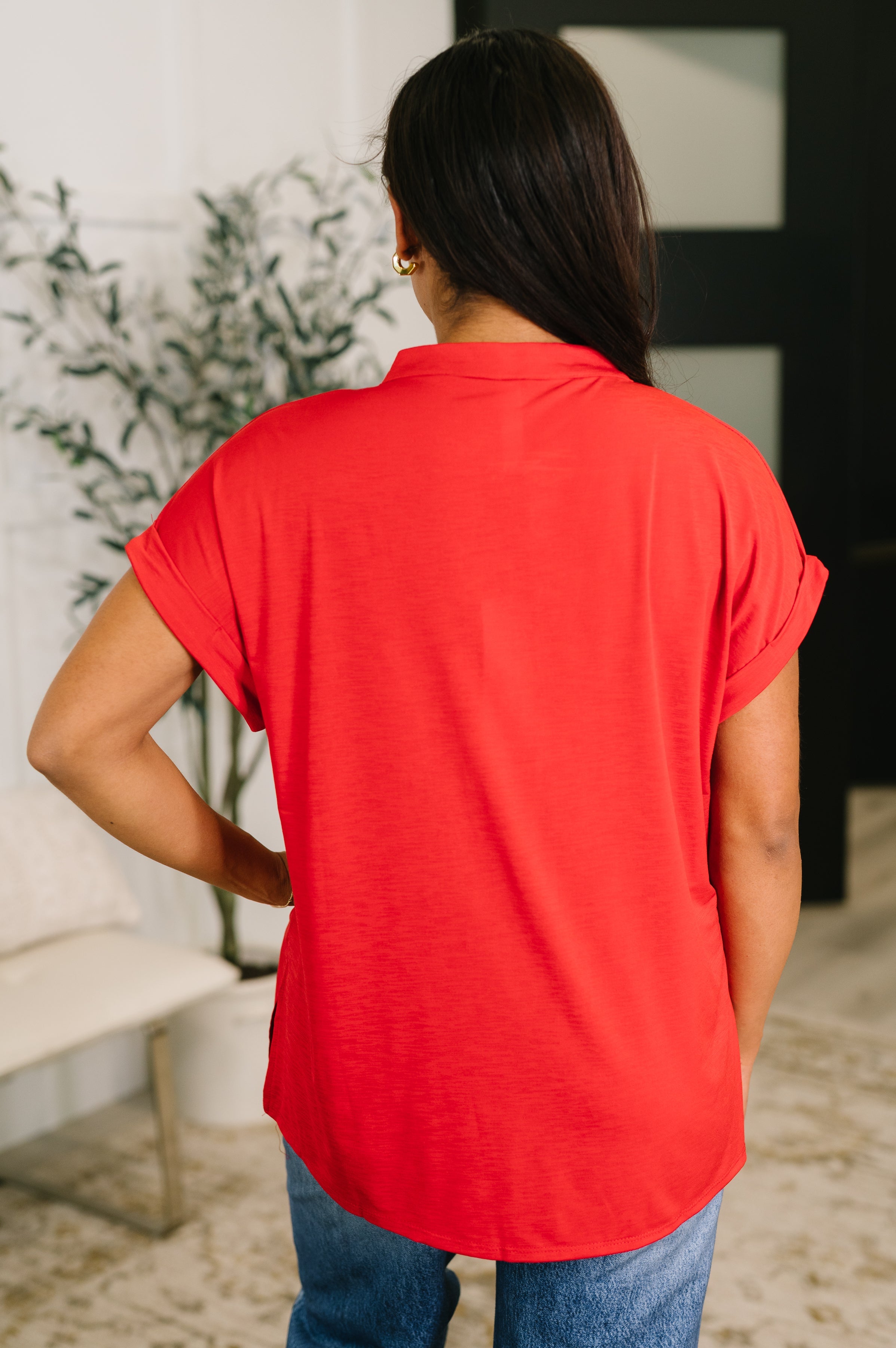 Back view of a red split neck blouse with rolled sleeves worn casually indoors by a woman with dark hair
