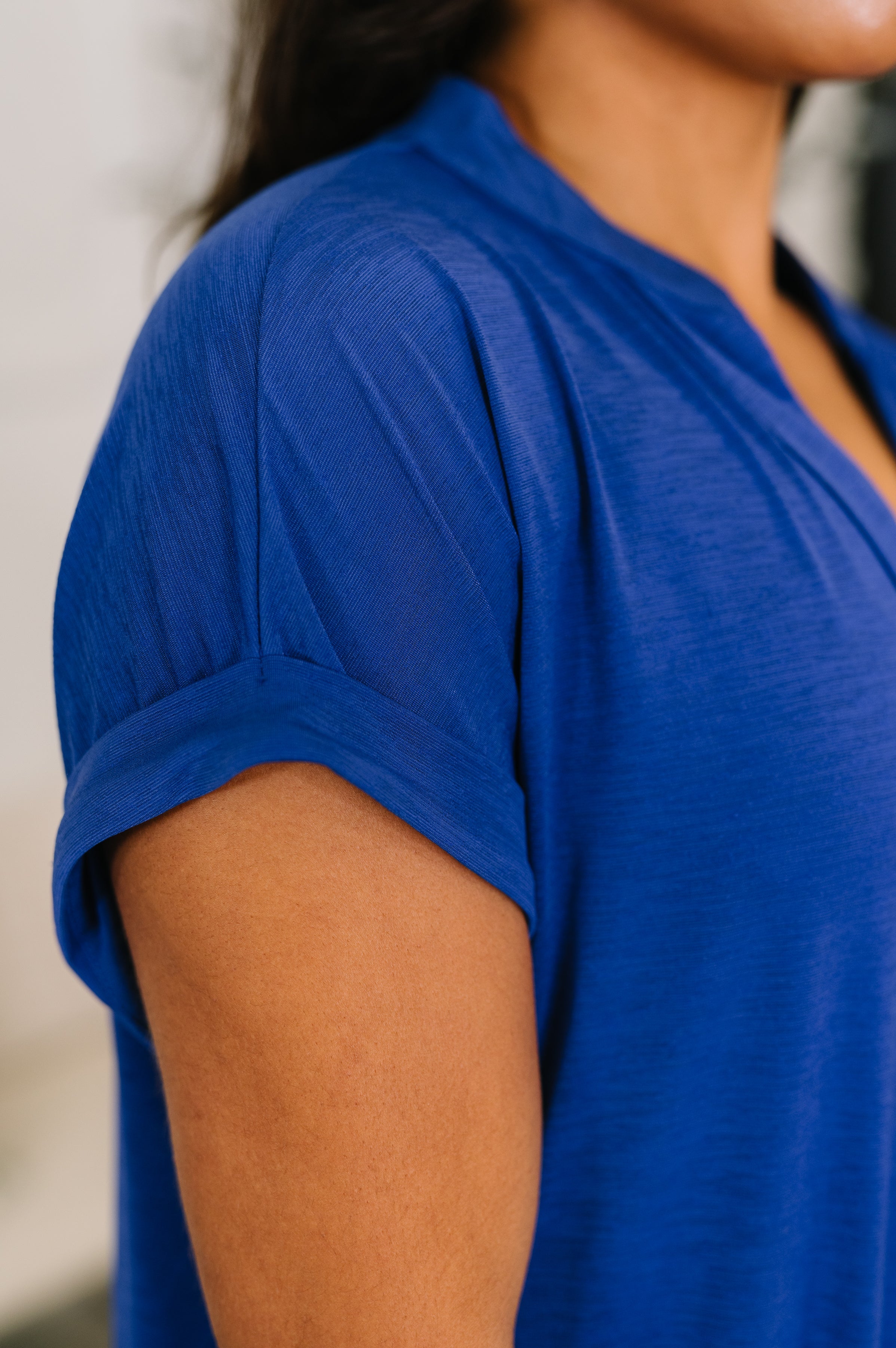 Close-up of royal blue blouse sleeve with rolled cuff and soft textured fabric on model's arm