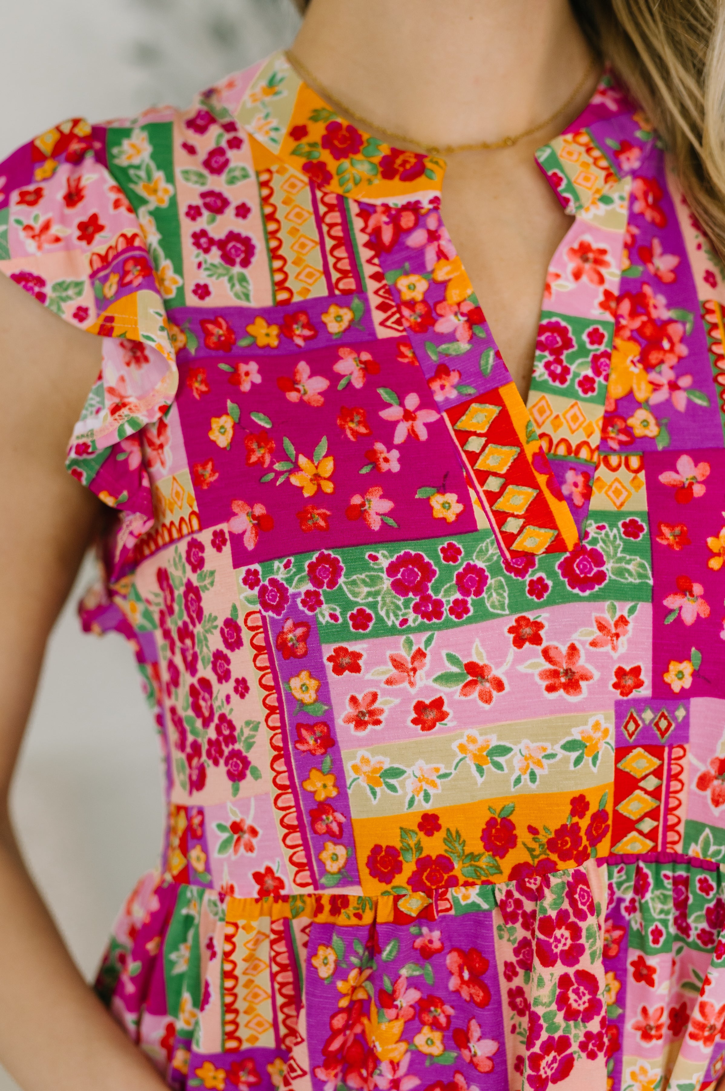 Close-up of fuchsia patchwork floral dress with flutter sleeves, gathered tiers, and V-neckline in soft fabric