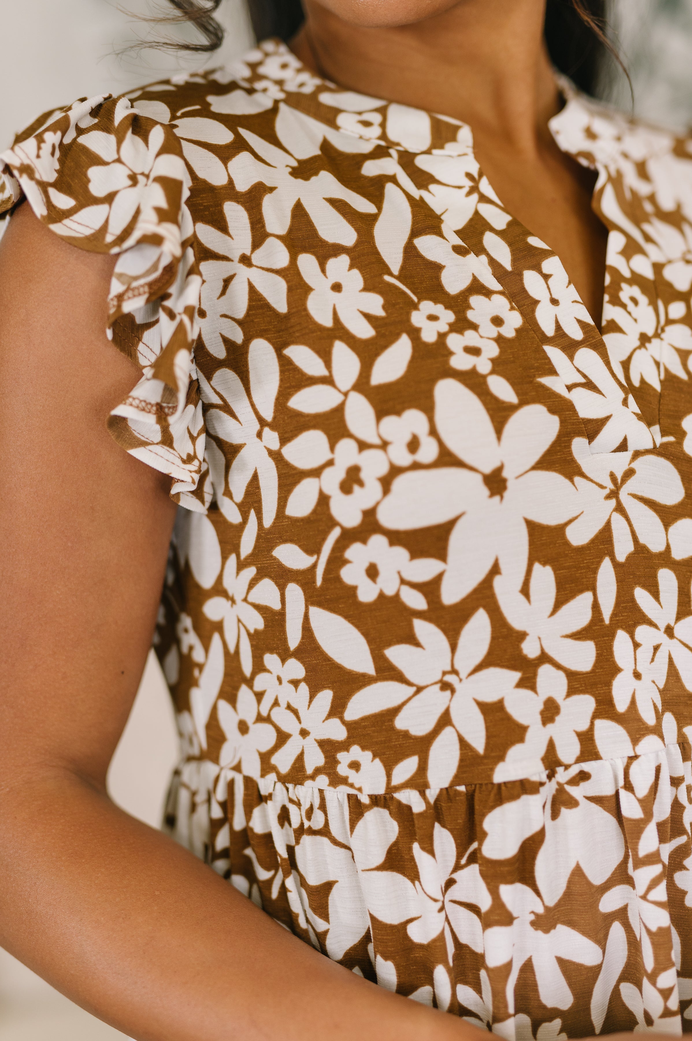 Close-up of a woman wearing a mocha dress with white floral print and delicate flutter sleeves
