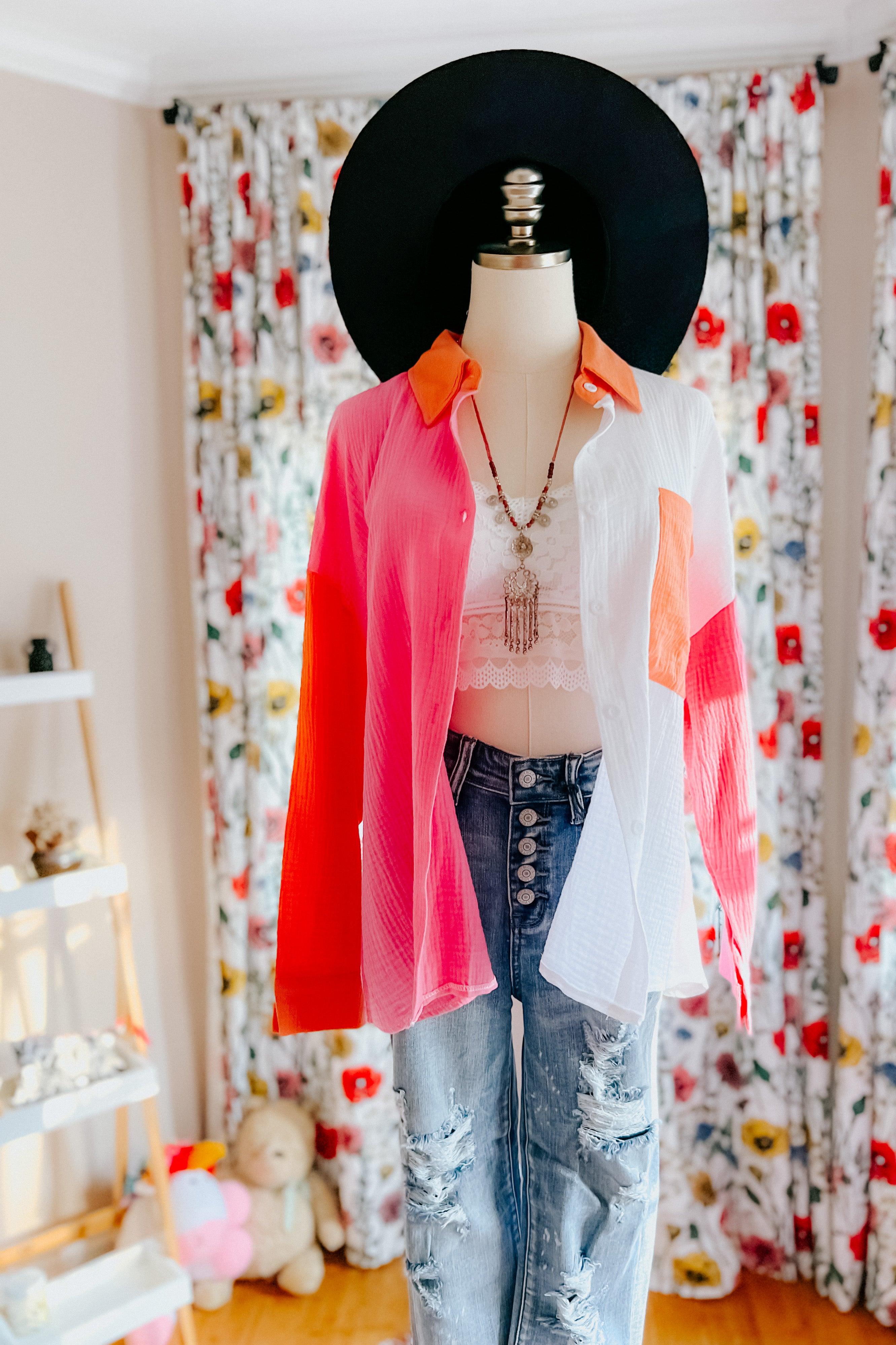 Mannequin dressed in pink, orange, and ivory color block top with distressed jeans and black wide-brim hat indoors