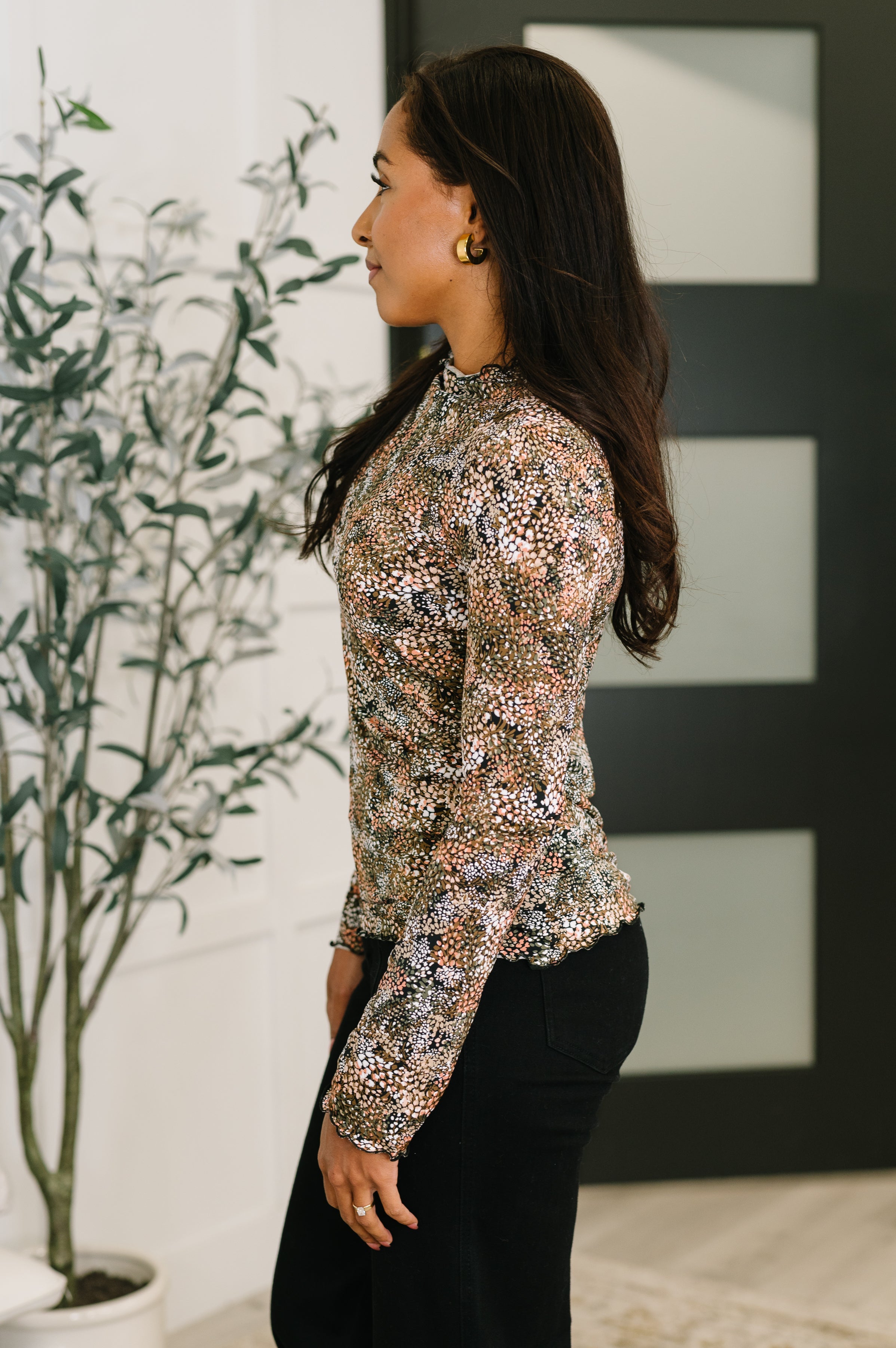 Woman wearing a fitted long-sleeve top with a small floral pattern in neutral tones paired with black pants indoors