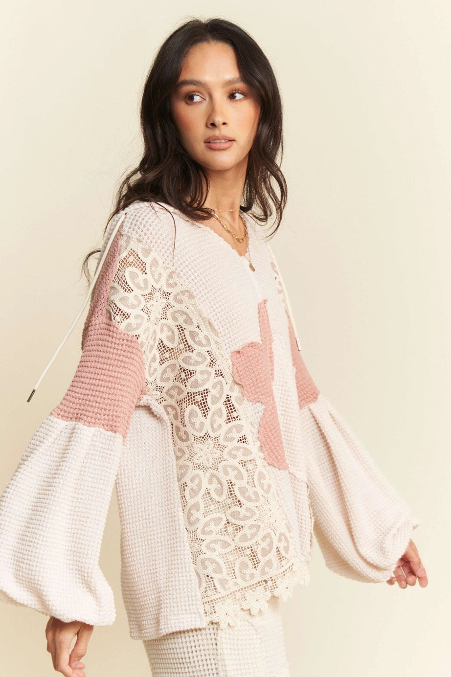 Cream waffle knit top with puffed sleeves and intricate lace panel worn by woman with long dark hair