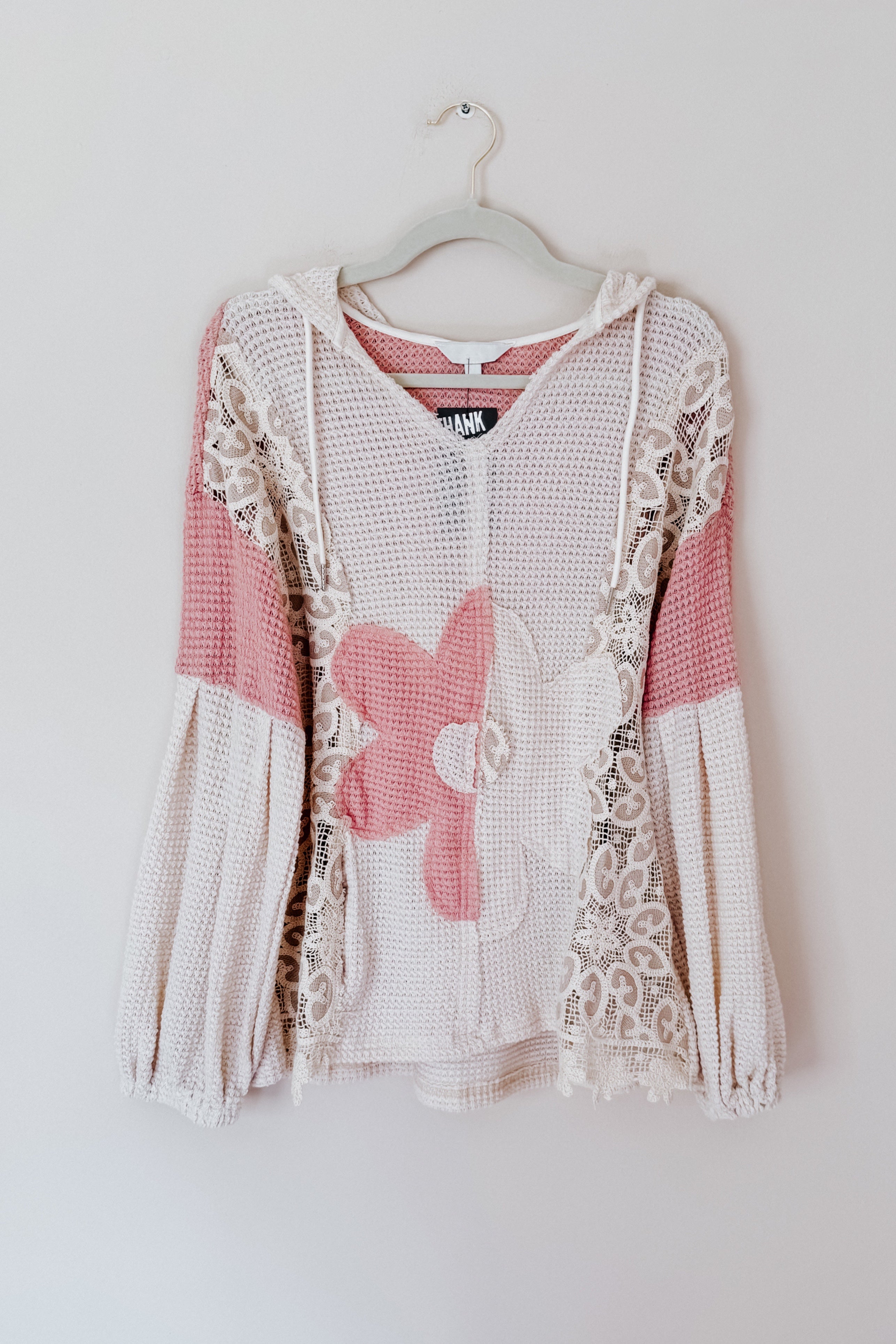 Cream waffle knit hooded top with balloon sleeves featuring pink floral patches and lace trim hanging on white hanger