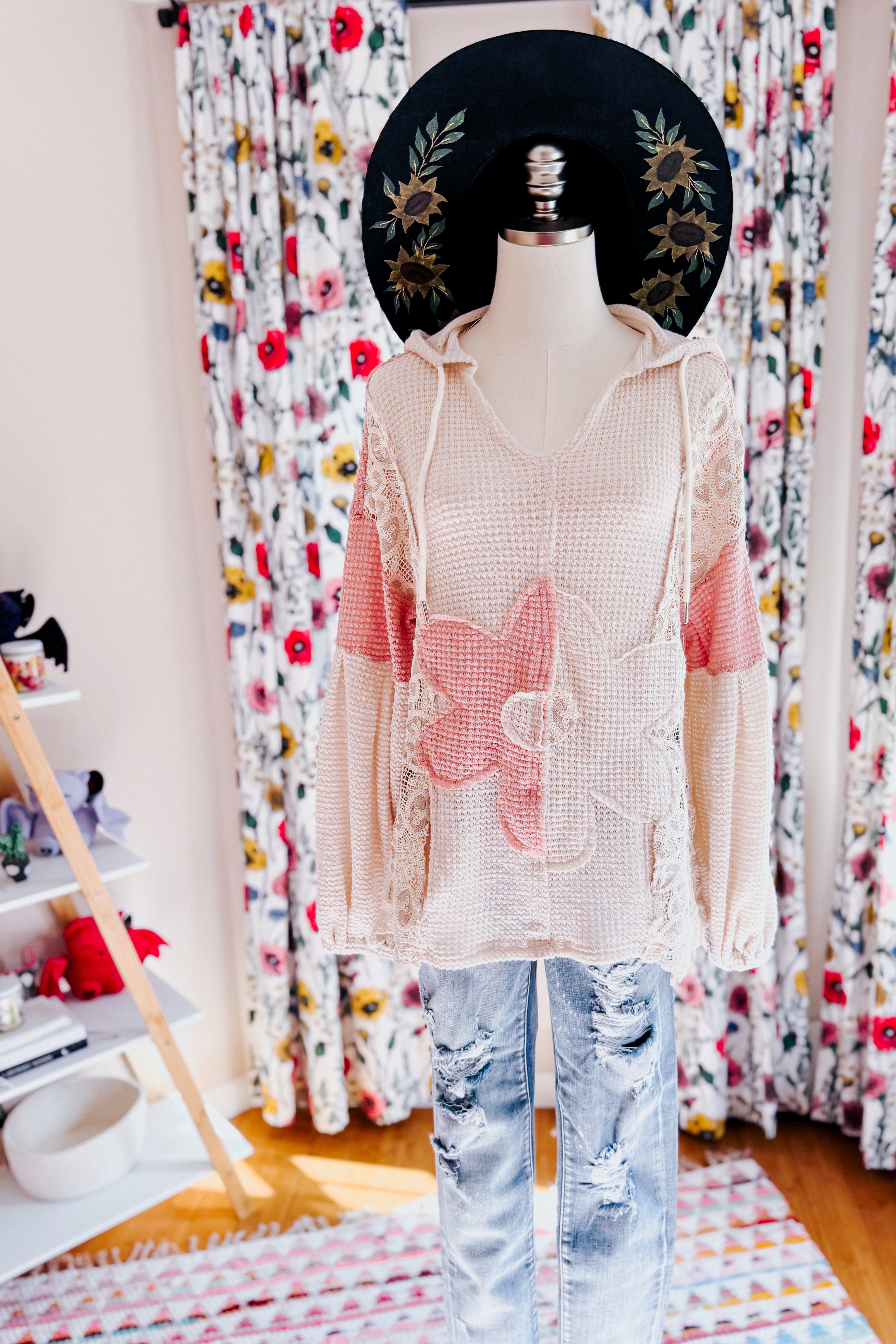 Cream waffle knit hoodie with large pink lace flower patches paired with distressed light wash jeans and black floral hat