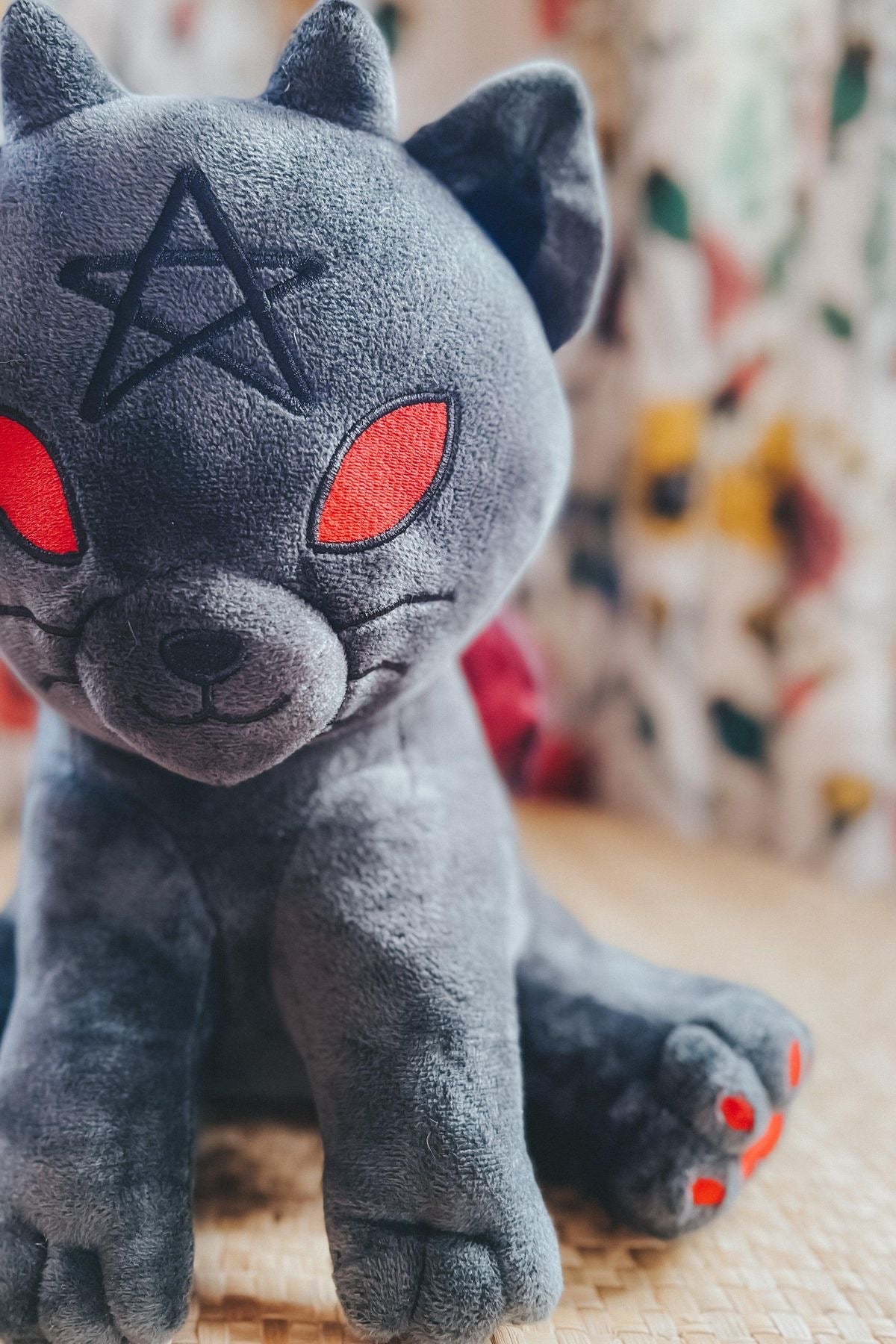 Charcoal black witchy kitten plush toy with red eyes pentagram marking and paw accents seated on a wooden surface
