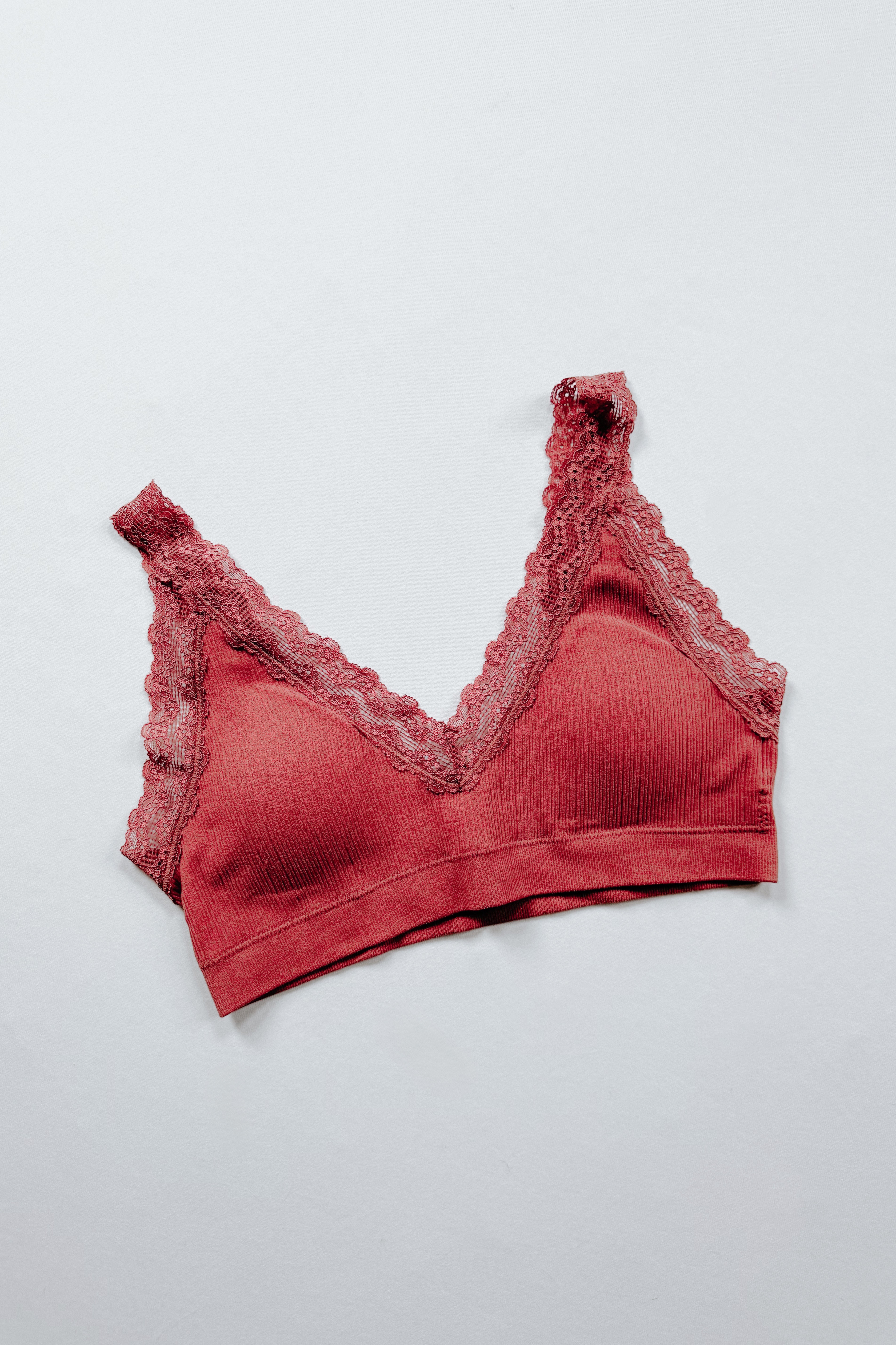 Rust-colored ribbed bralette featuring scalloped lace trim along the neckline and straps laid flat on light background