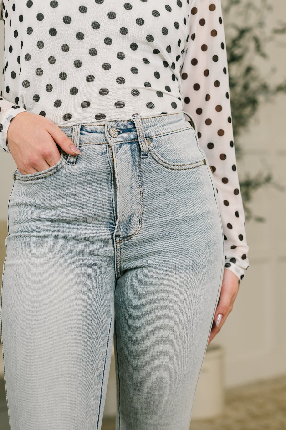 Close view of light wash blue high waist jeans with a tummy control fit styled with a white polka dot blouse