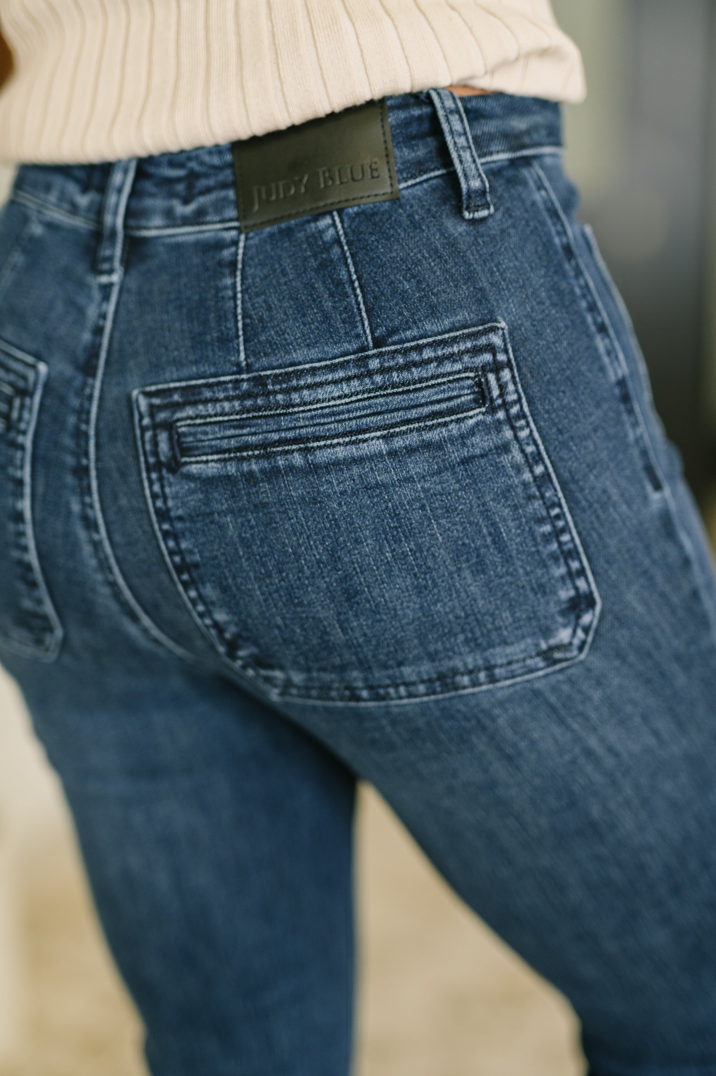 Close-up of back view showing vintage pockets on high waist Mackenzie flare jeans in dark blue denim indoors