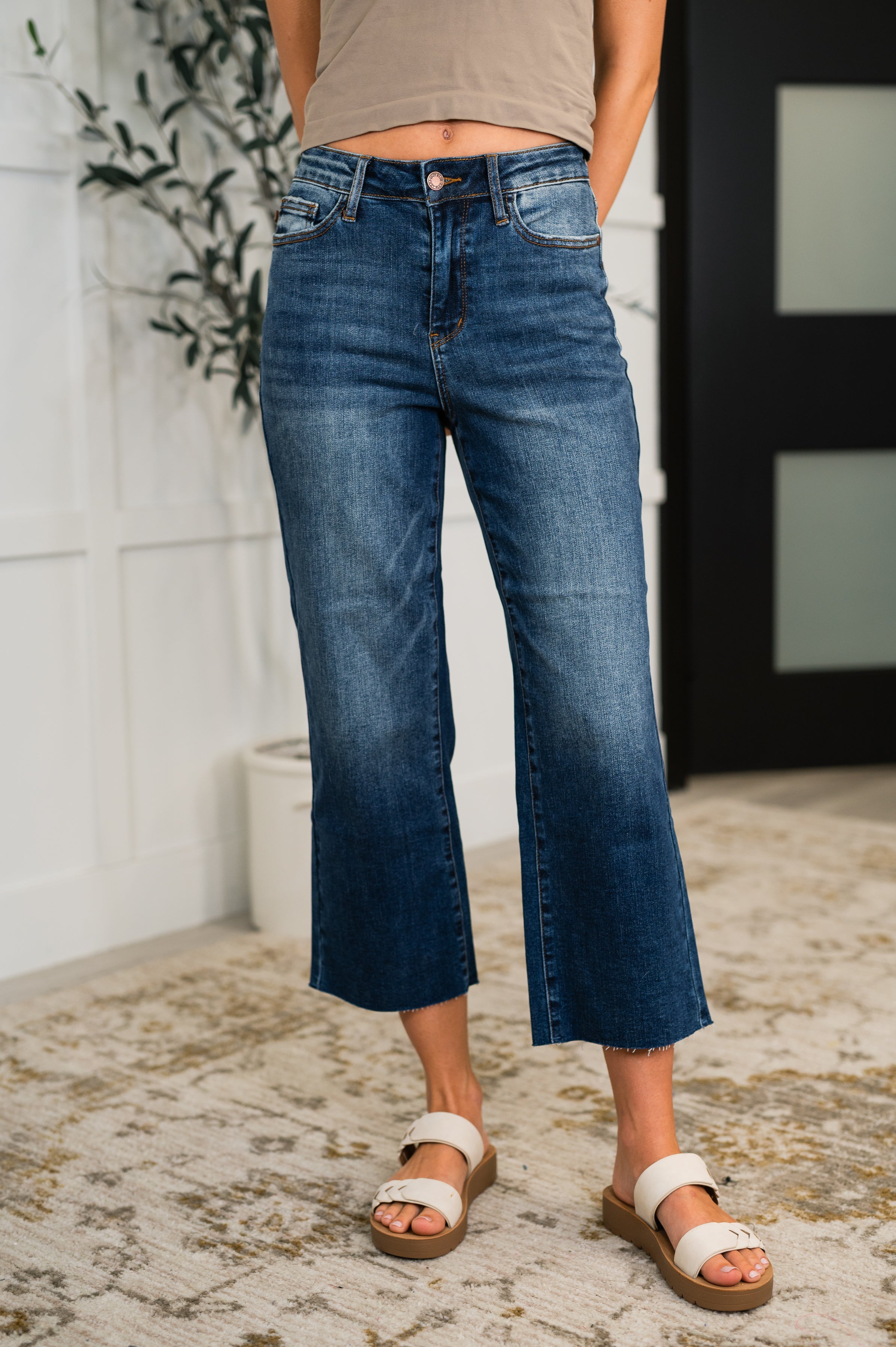 Mid-rise blue denim wide-leg jeans with raw hem paired with white double-strap sandals on patterned rug