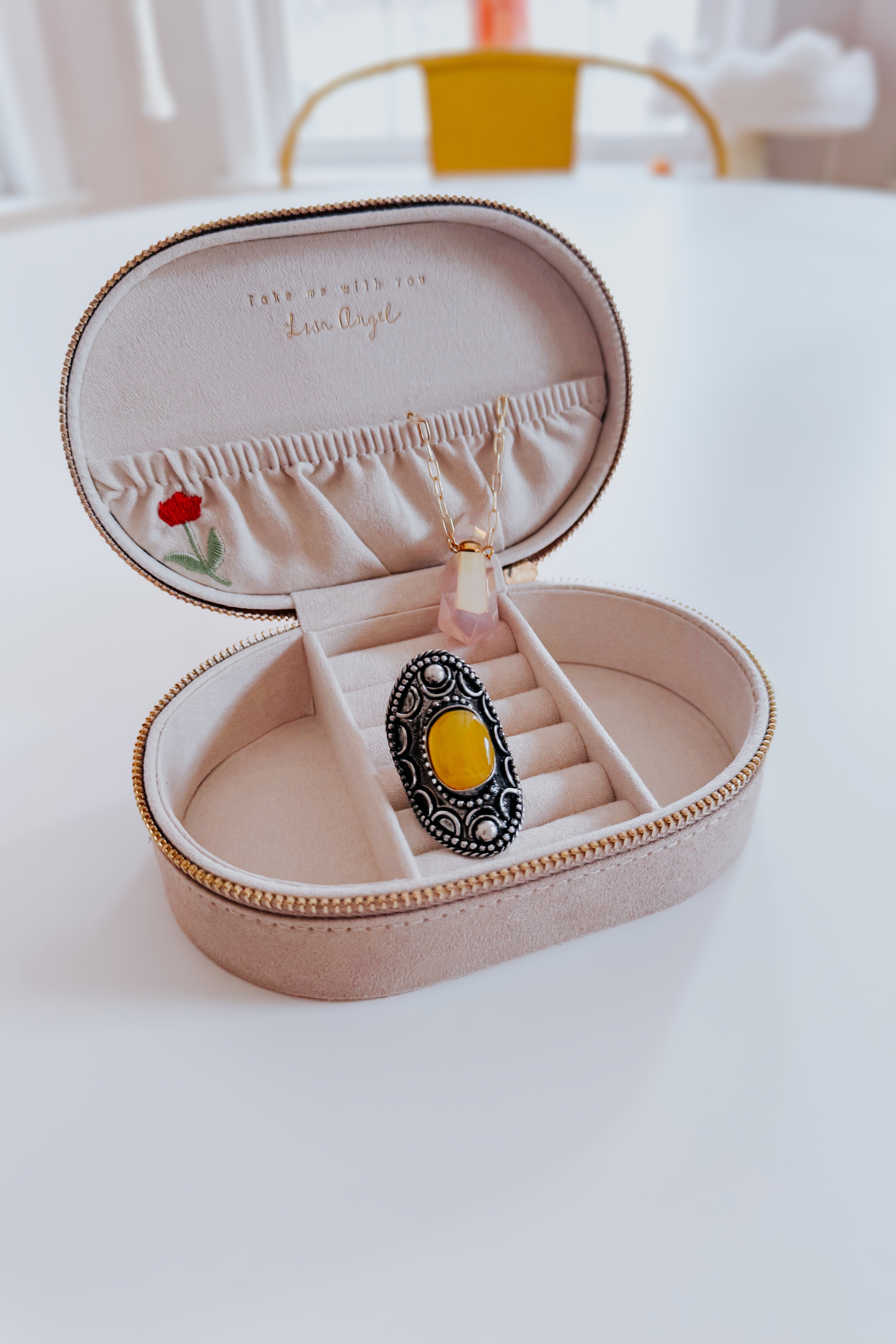 Cream velvet jewelry box with delicate floral embroidery holding a pendant and a decorative ring on white surface