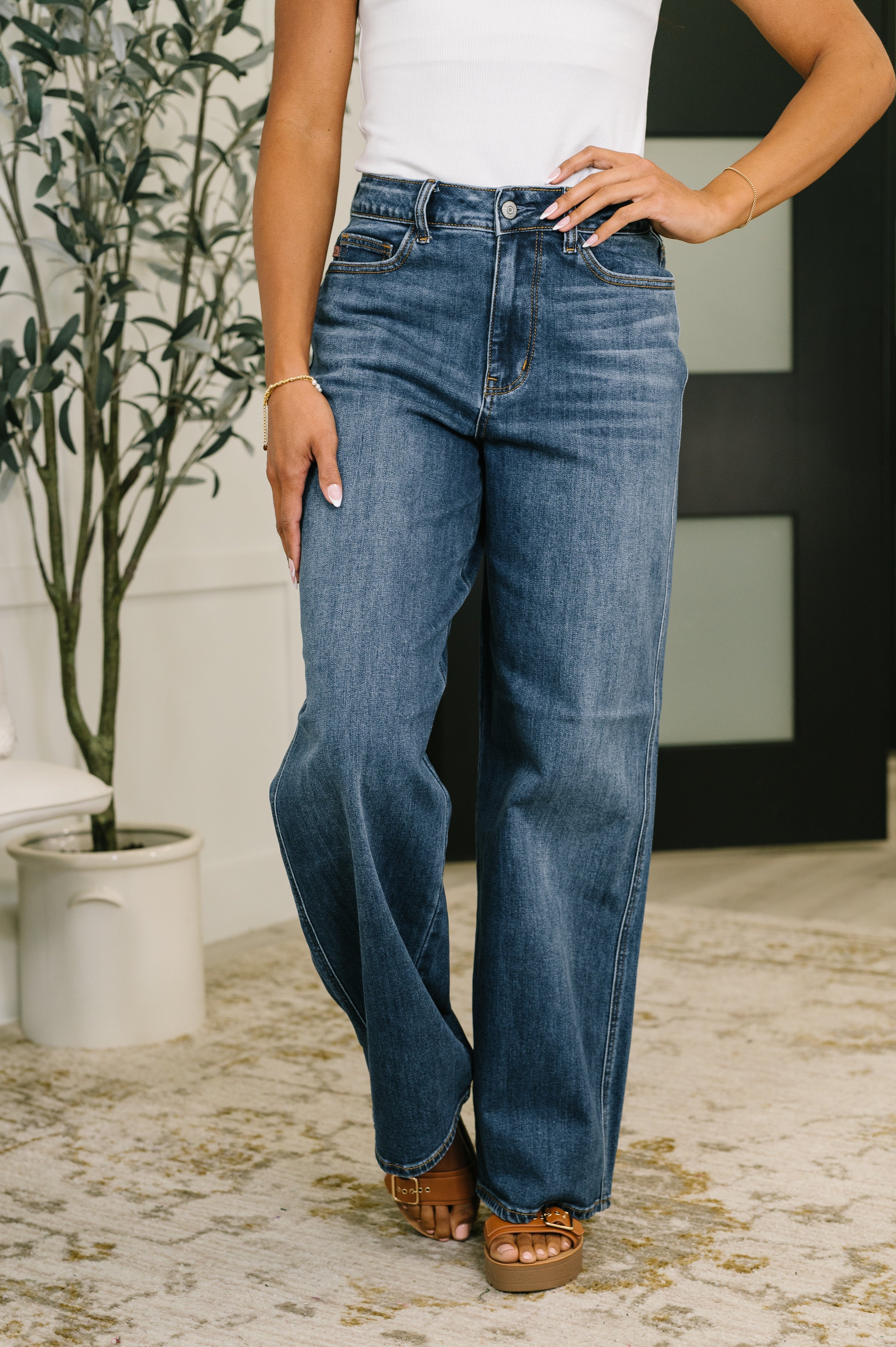 Woman wearing high waist Wilhelmina baggy jeans in medium blue wash with brown sandals indoors