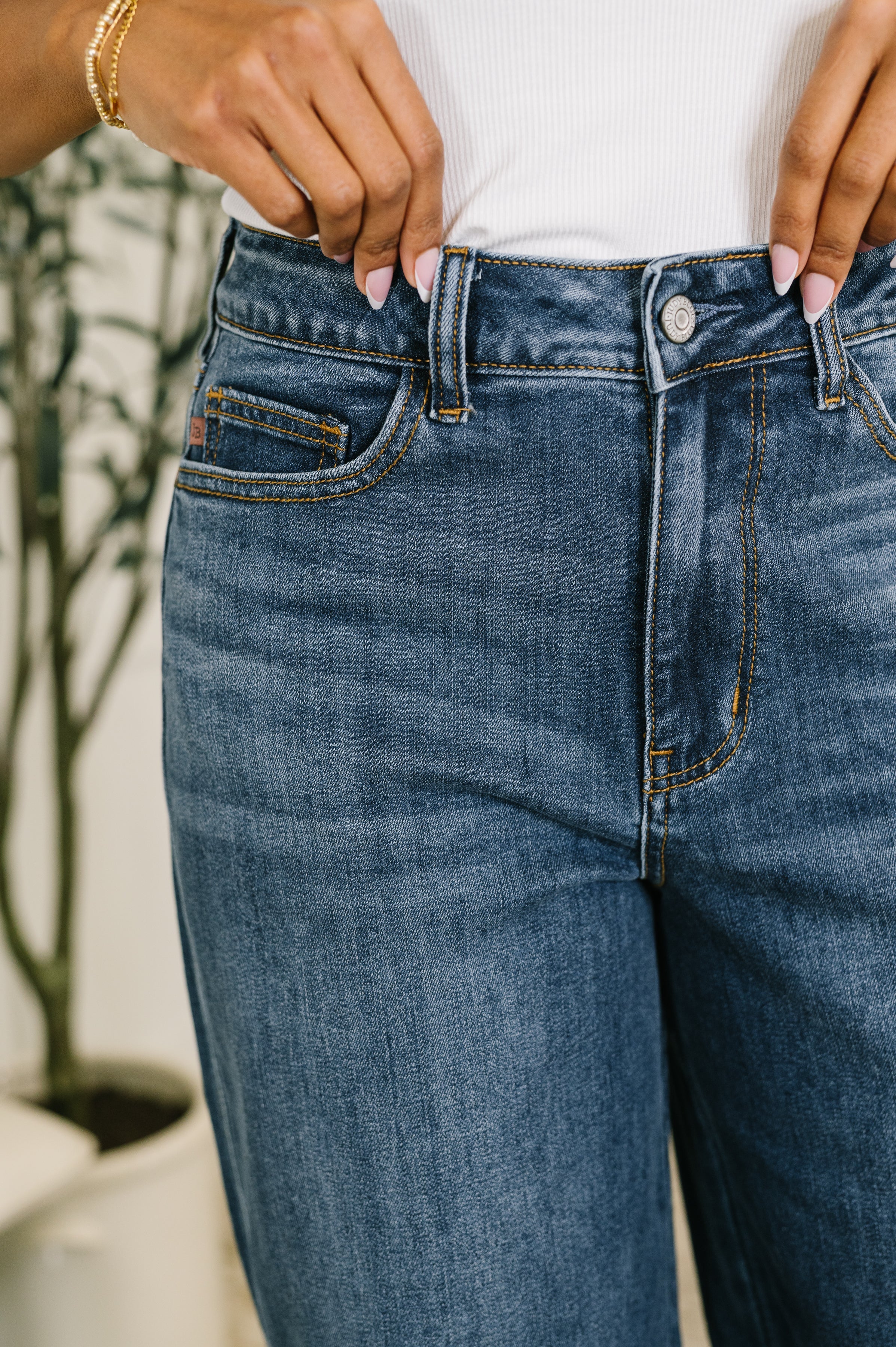 Close-up of woman adjusting button on high waist faded blue baggy jeans with contrast stitching indoors