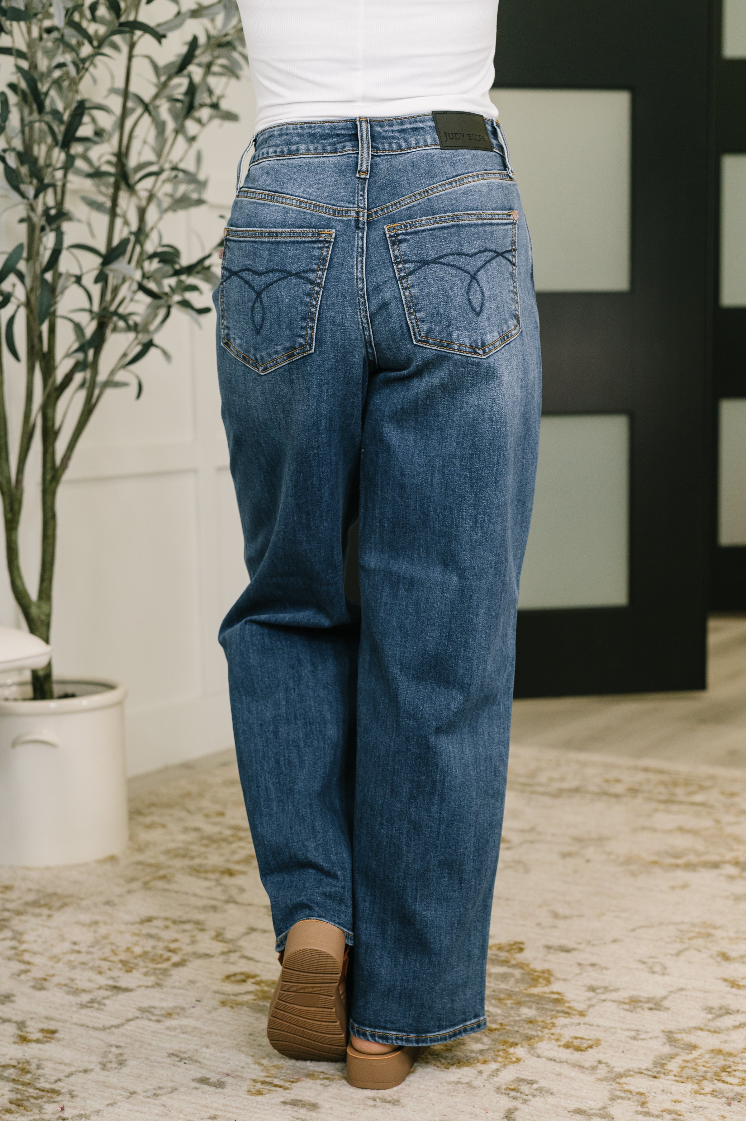 Back view of woman wearing Marie high waist Wilhelmina baggy blue jeans paired with tan shoes indoors