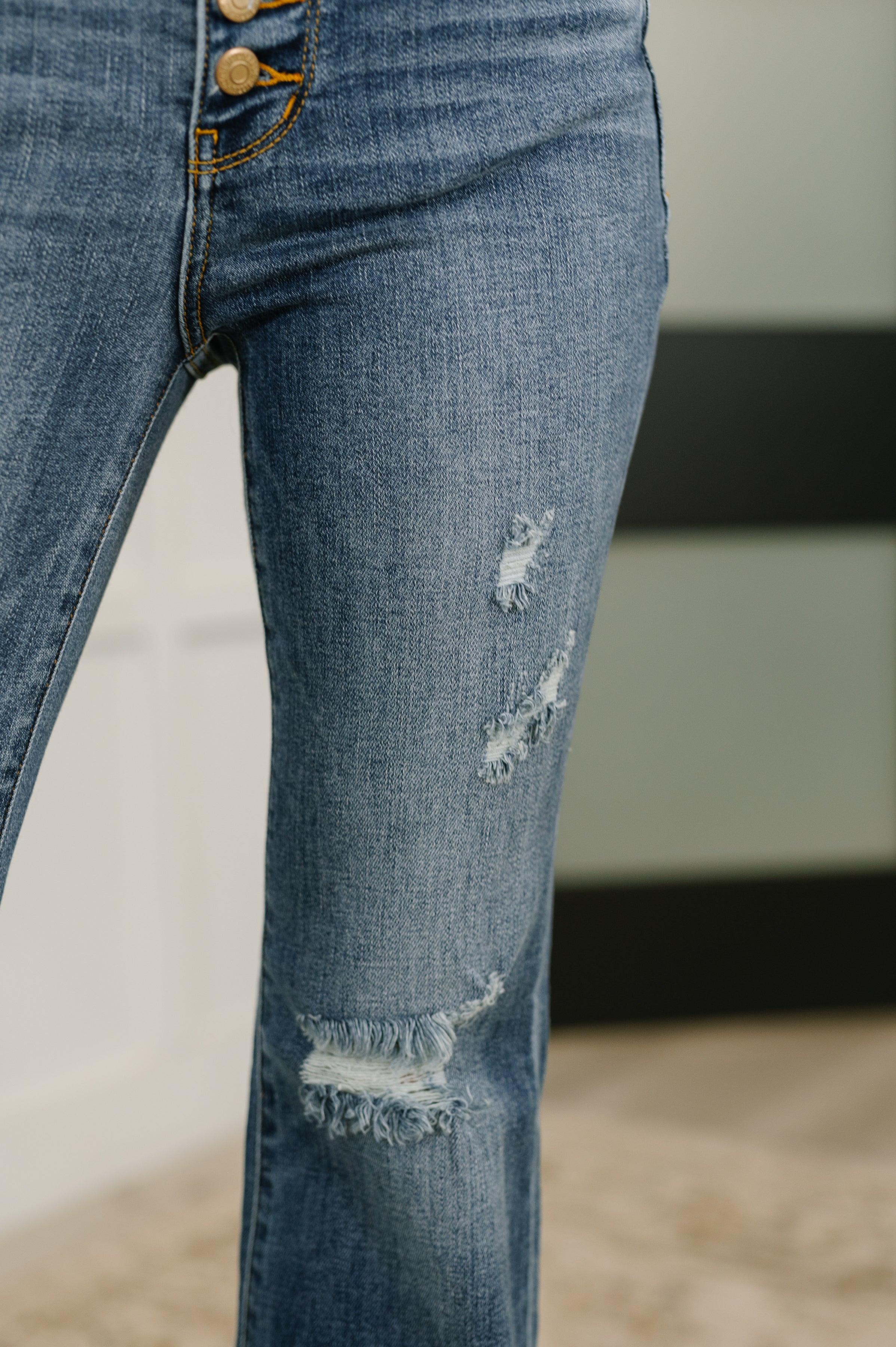Close-up of blue denim flare jeans with button fly and distressed frayed patches on thigh and knee areas