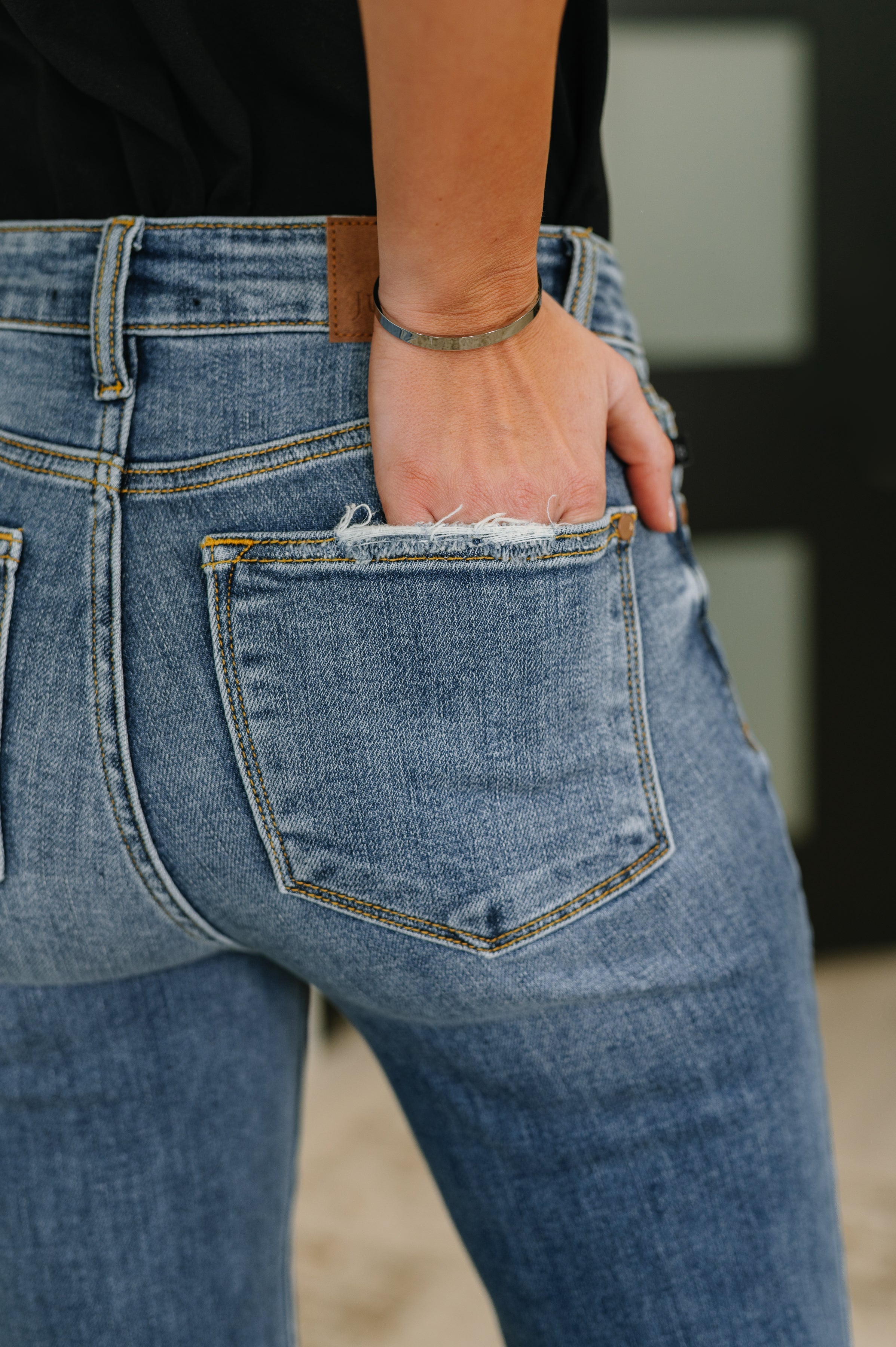 Close-up of blue mid-rise jeans with subtle frayed detailing on the back pocket and a hand resting inside the pocket