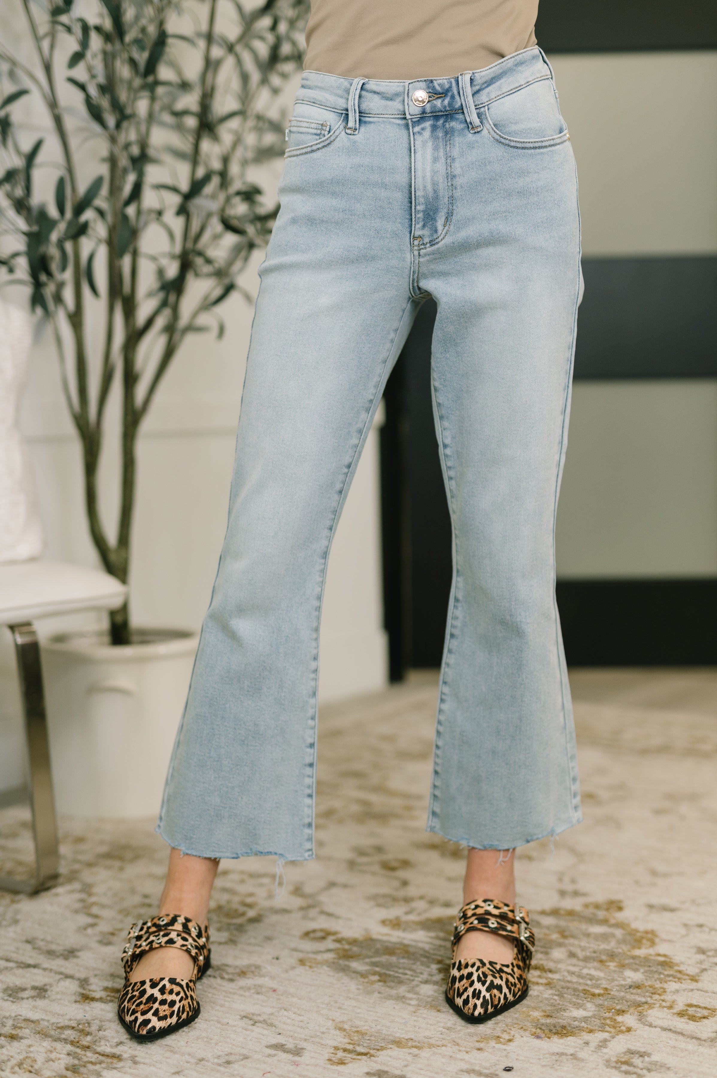 Light wash mid rise kick flare jeans with subtle fading and raw frayed hems paired with leopard print flats indoors