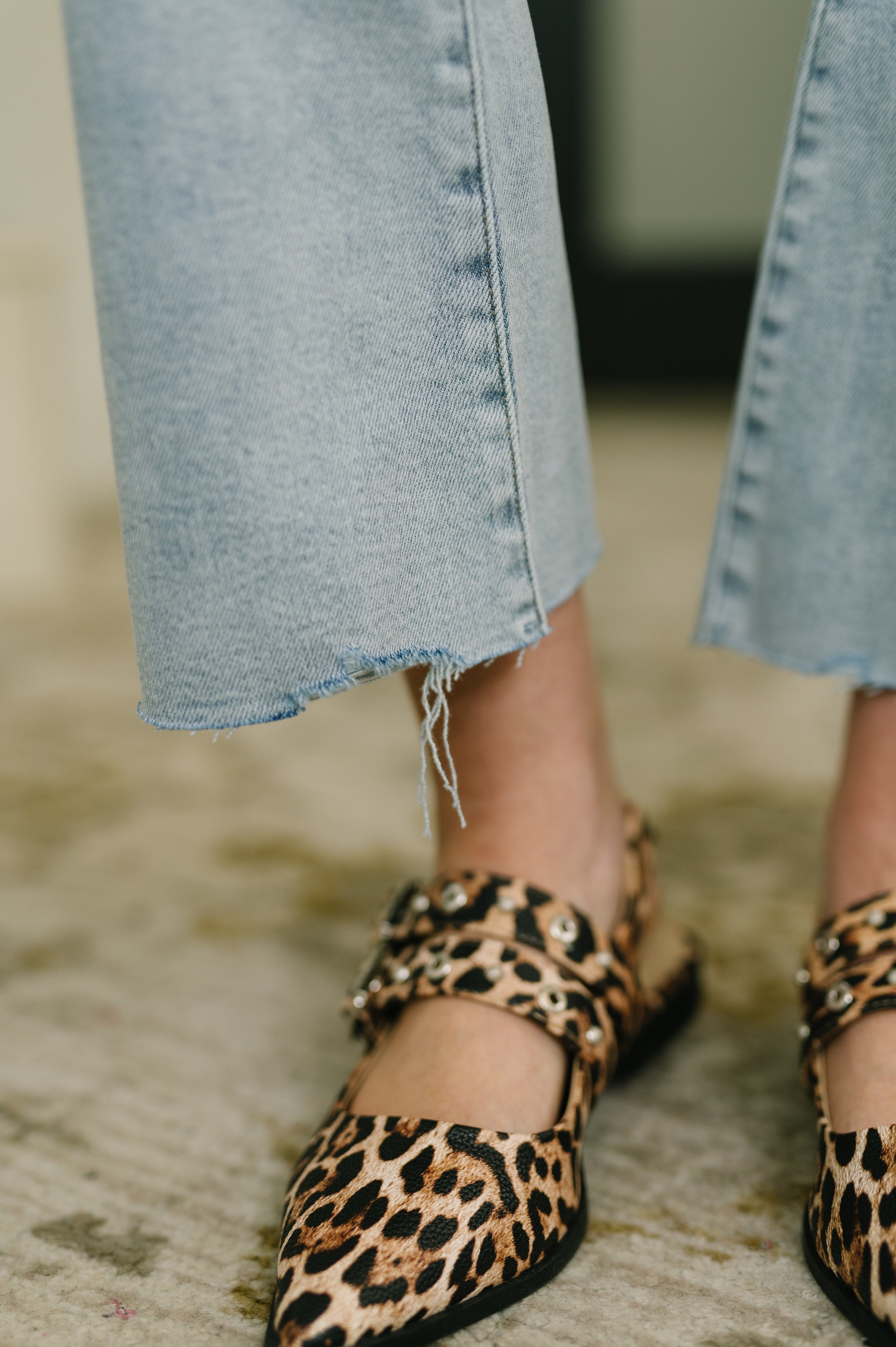 Close-up of light blue mid-rise kick flare jeans with frayed raw hems paired with leopard print pointed flats indoors