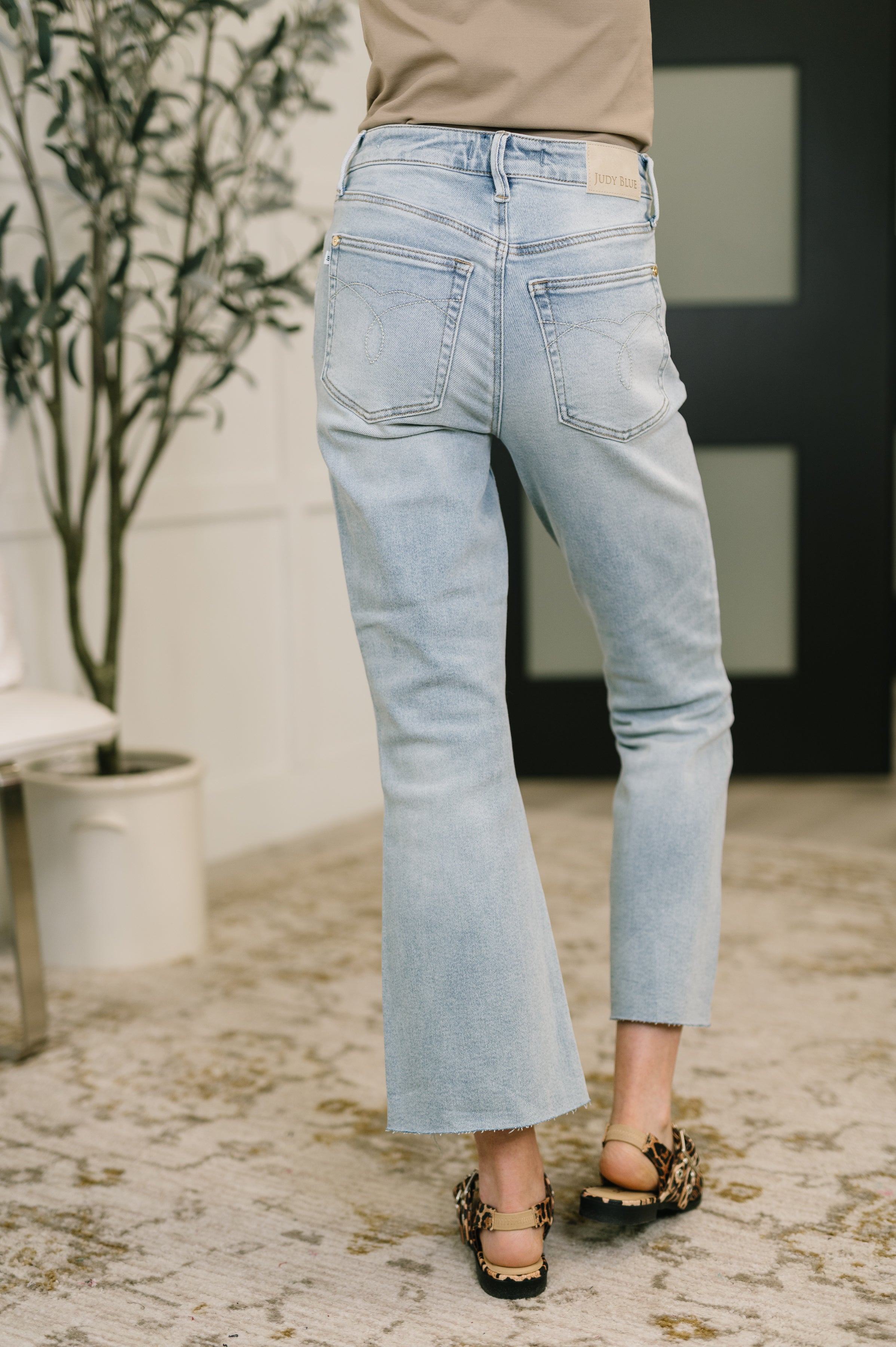 Woman wearing light wash mid-rise kick flare jeans with raw hem and leopard print sandals indoors