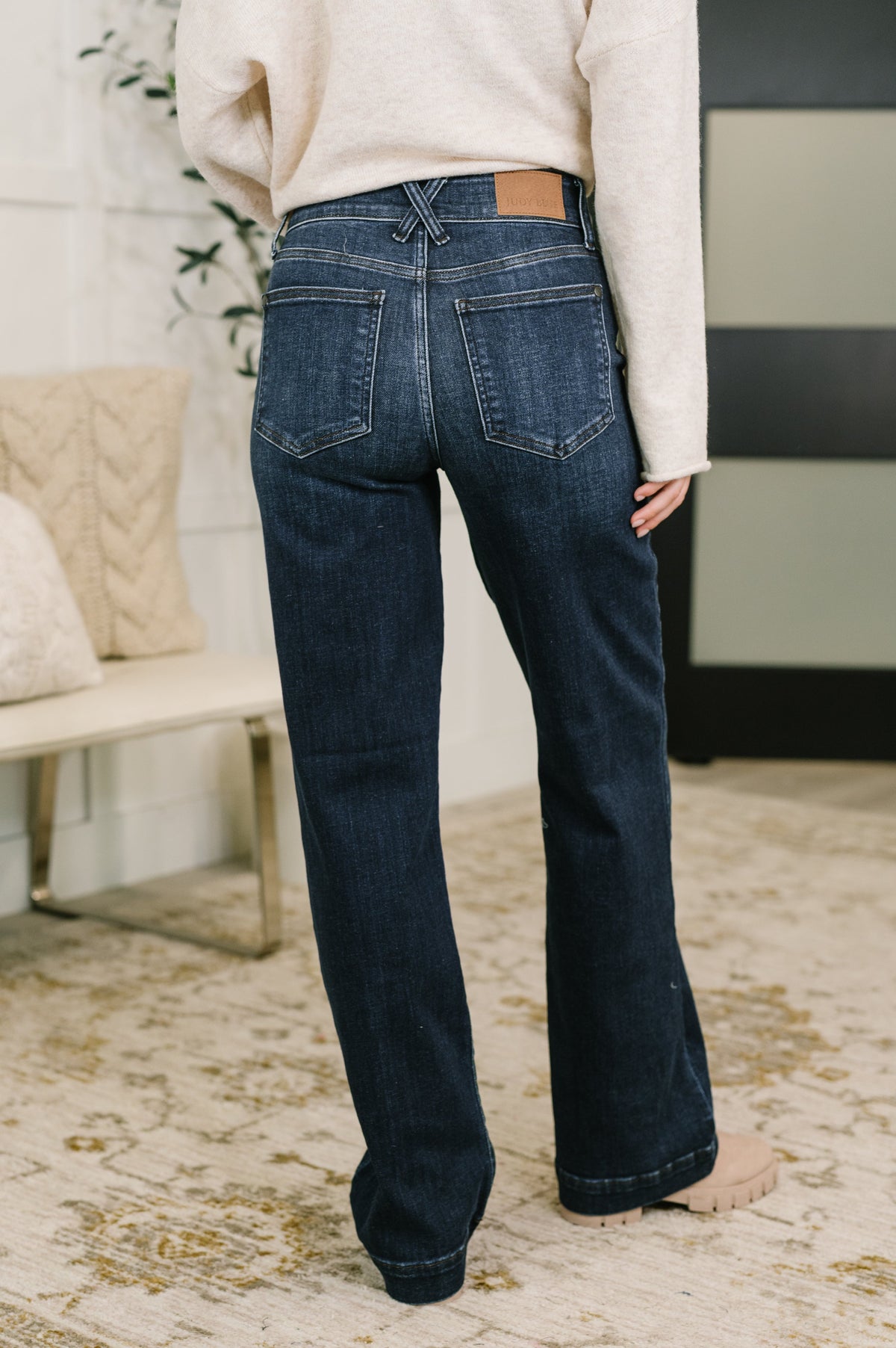 Rear view of a woman wearing blue high waist wide leg jeans with a double button closure and cream sweater indoors