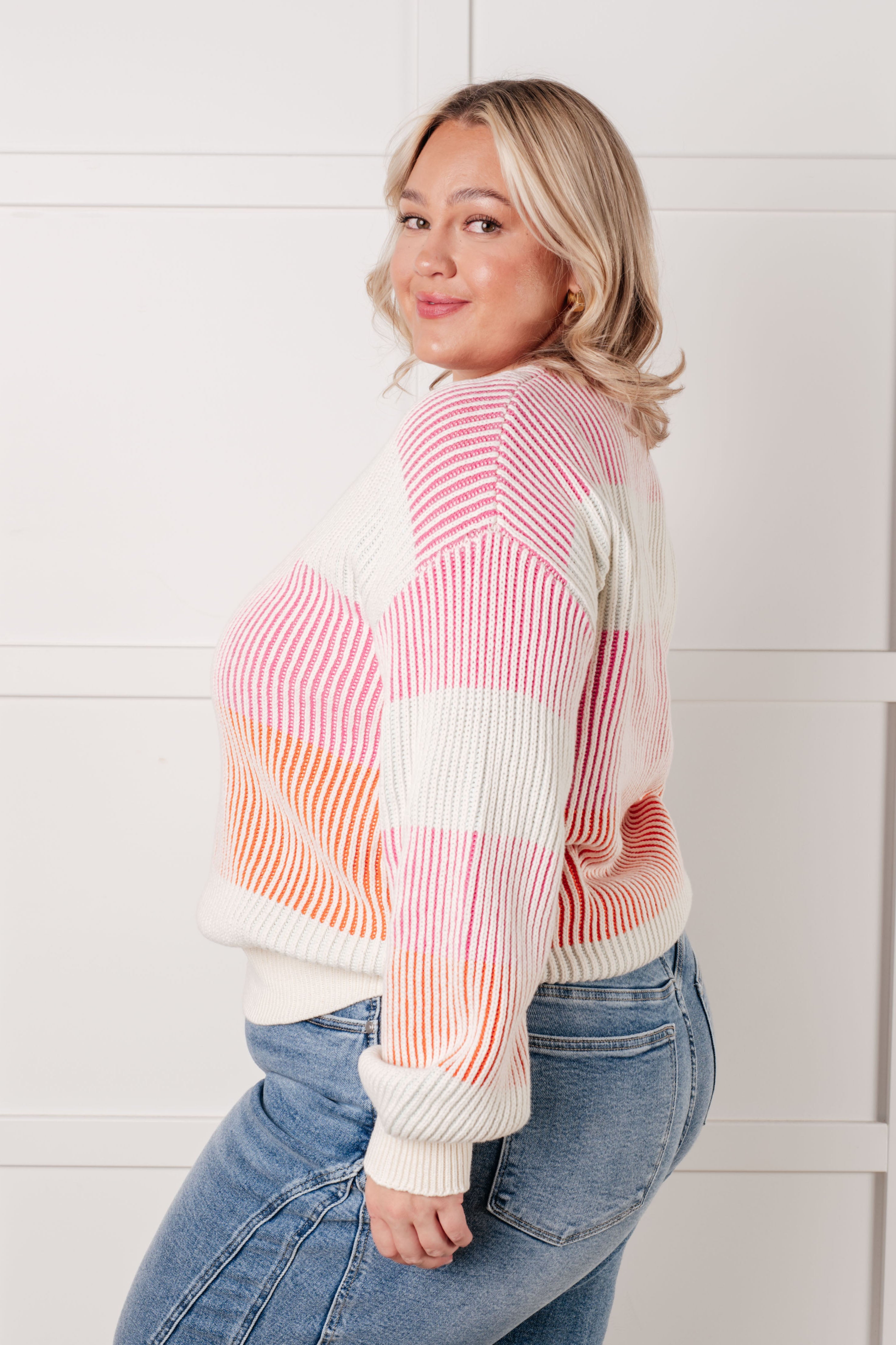 Woman wearing a ribbed striped top in pink, orange, and cream shades paired with light blue jeans indoors
