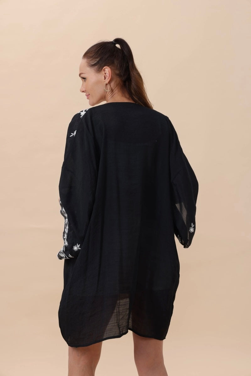 Woman wearing a black lightweight duster with white floral embroidery on the sleeves seen from behind